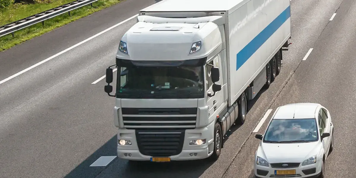 Een witte vrachtwagen en witte auto rijden op de snelweg naast elkaar