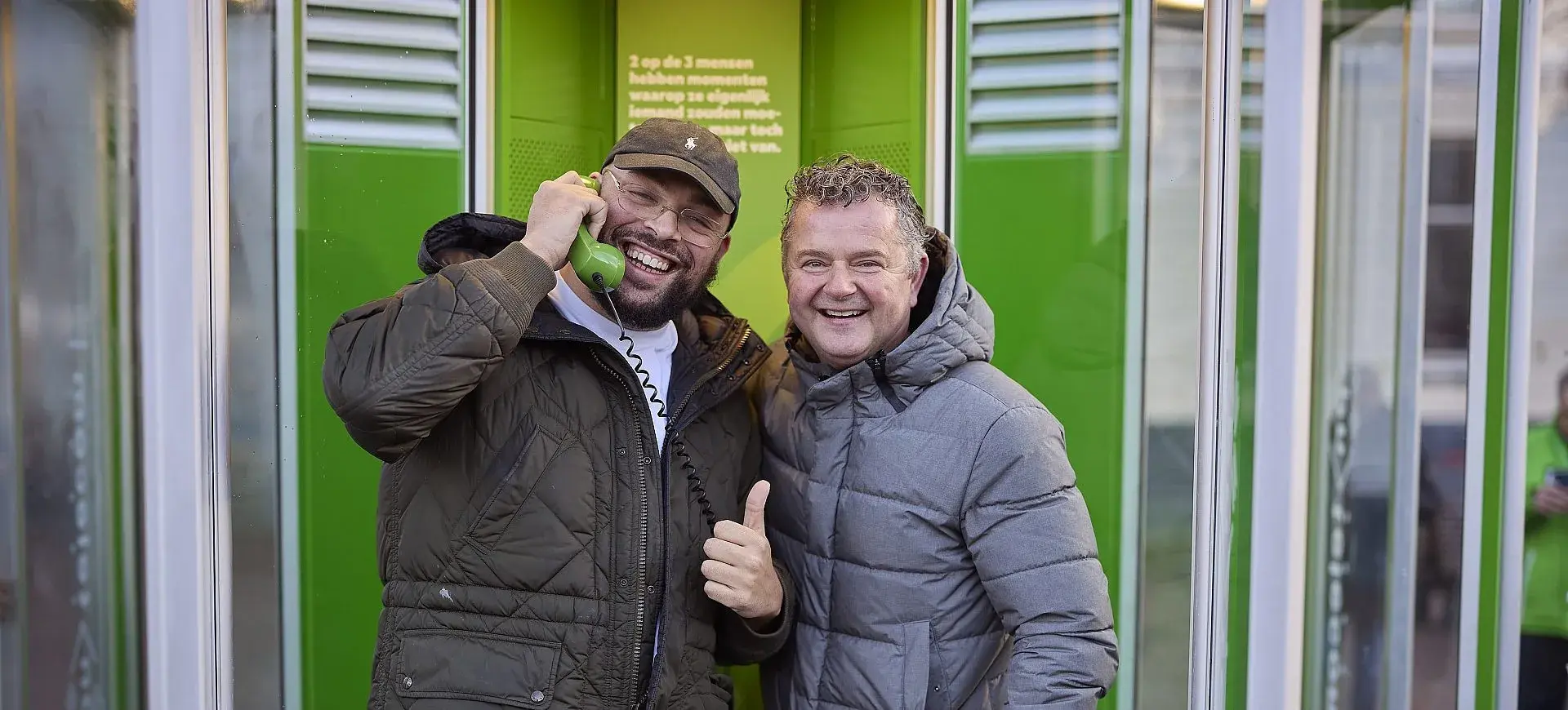 Twee mannen bij een KPN telefooncel met telefoonhoorn in de hand