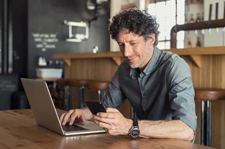 Man in een bar aan tafel met laptop en telefoon