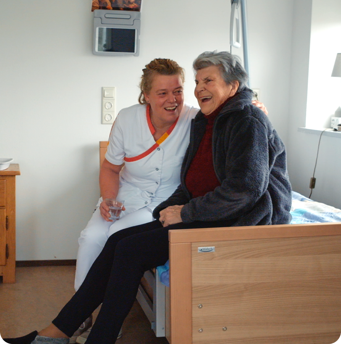 Verpleegkundige en patiënt zitten op een bed en lachen