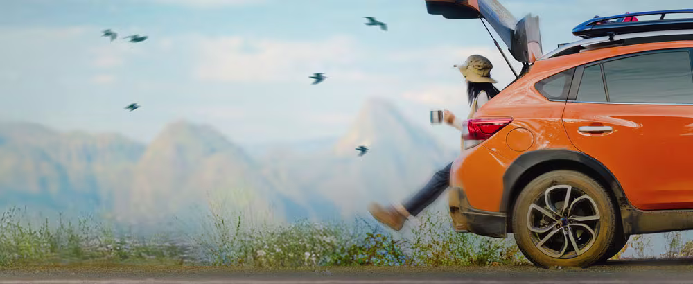 Woman sitting on car boot looking at mountains