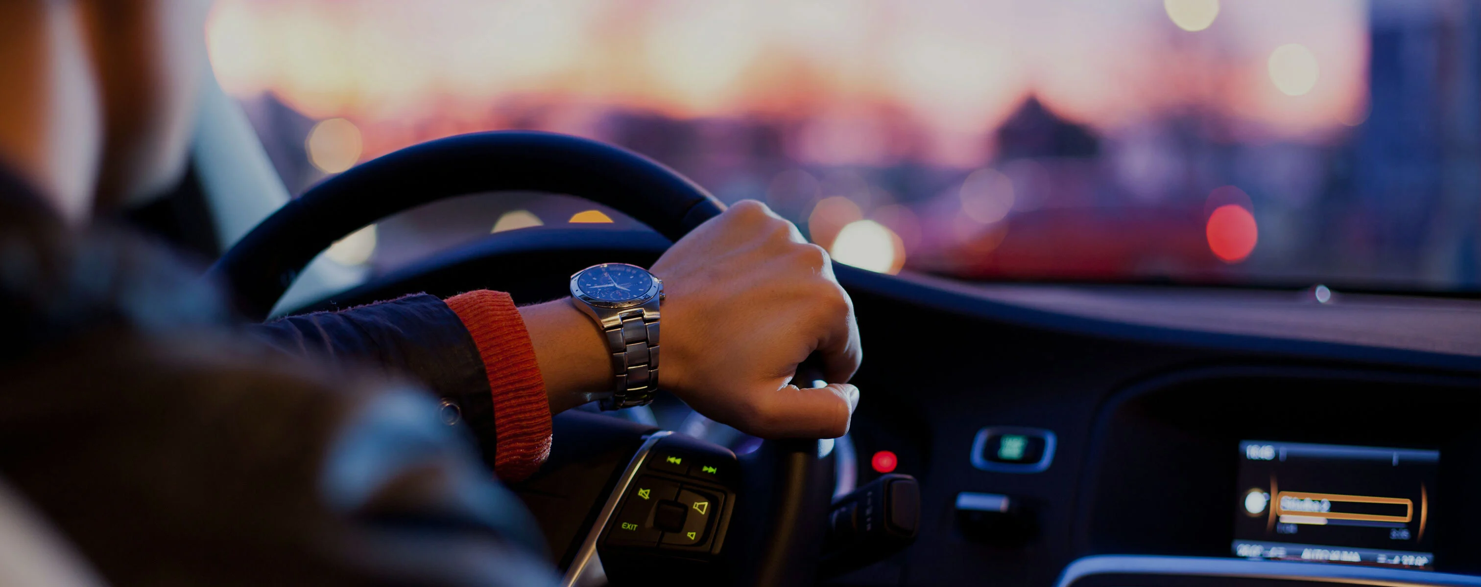 Person sitzt am Steuer eines Autos und fährt in der Dämmerung.