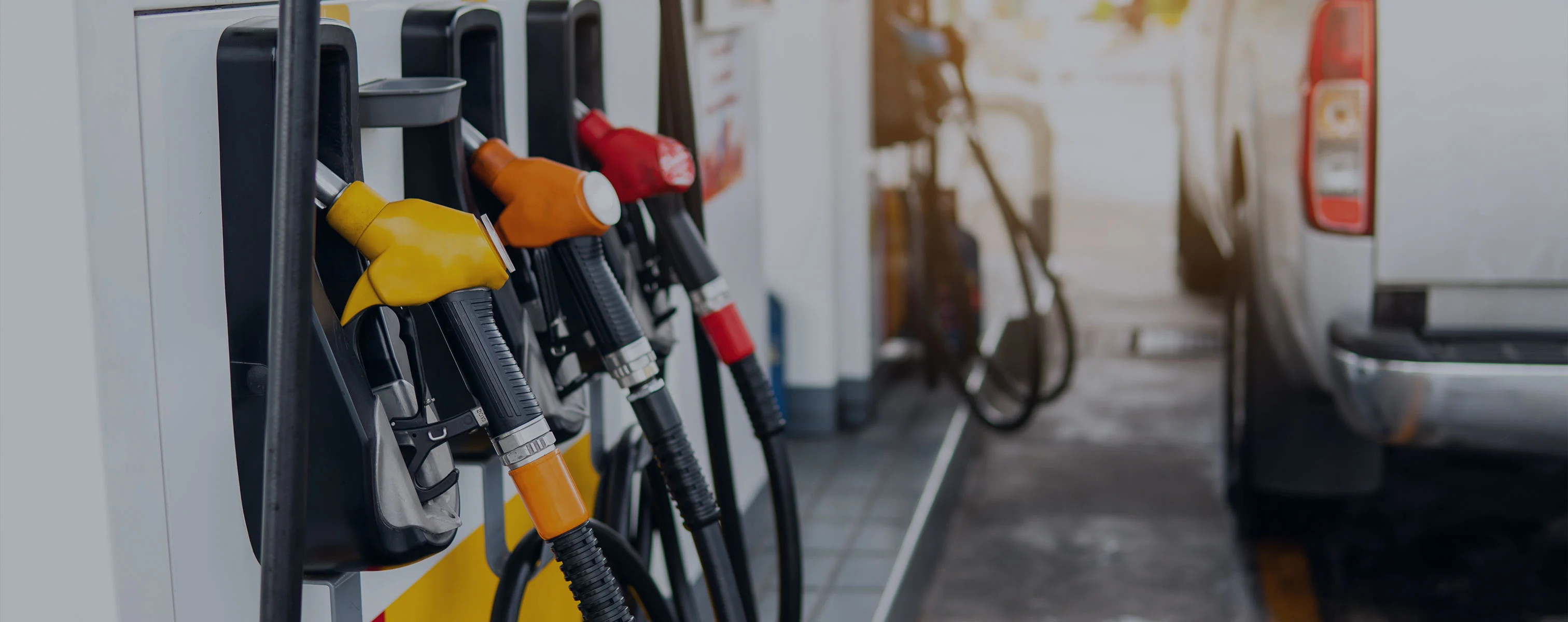 Zapfsäulen mit unterschiedlichen Kraftstoffpumpen an einer Tankstelle, ein Fahrzeug steht in der Nähe.