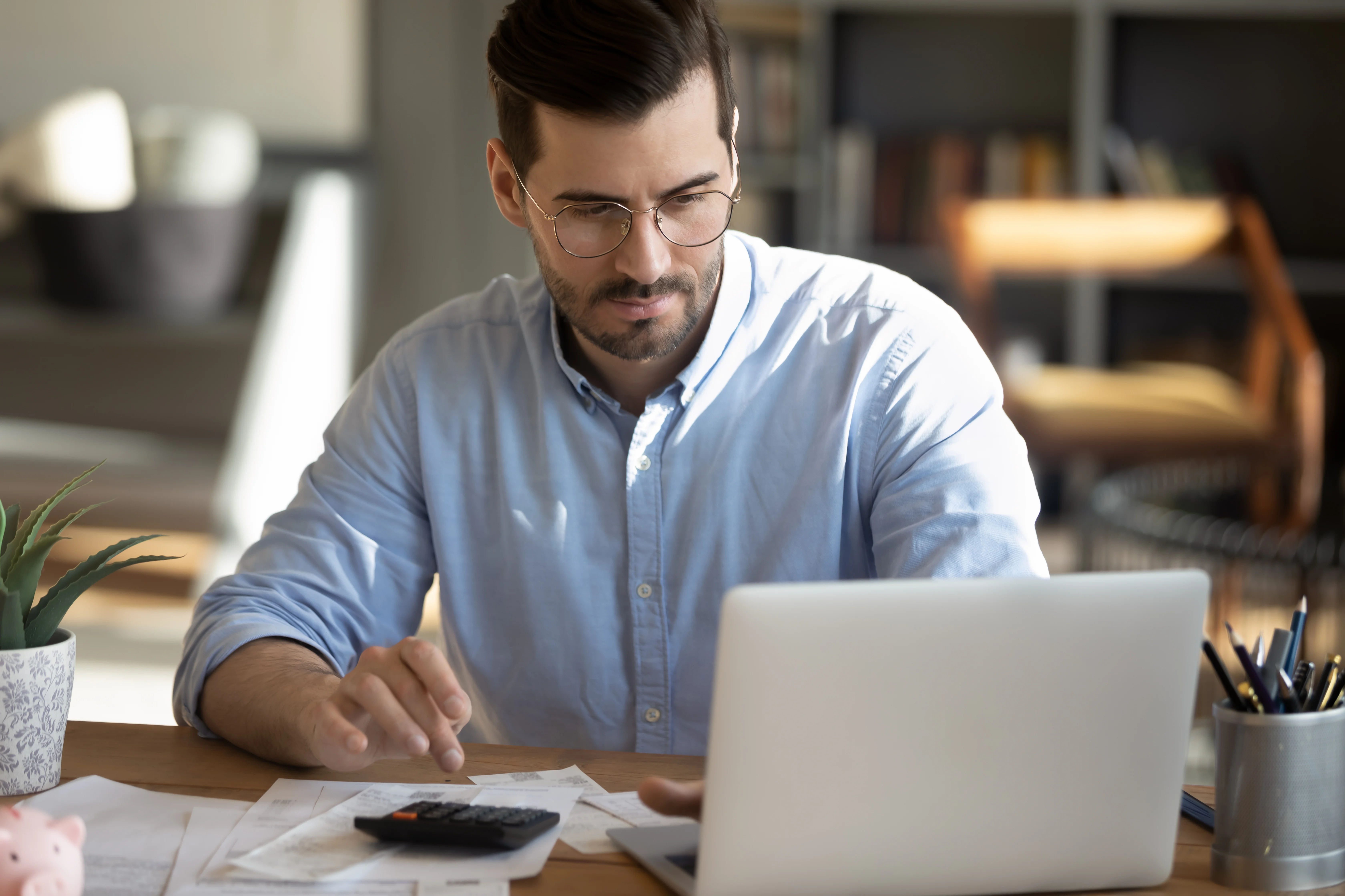 Mann arbeitet am Laptop mit Dokumenten und Taschenrechner