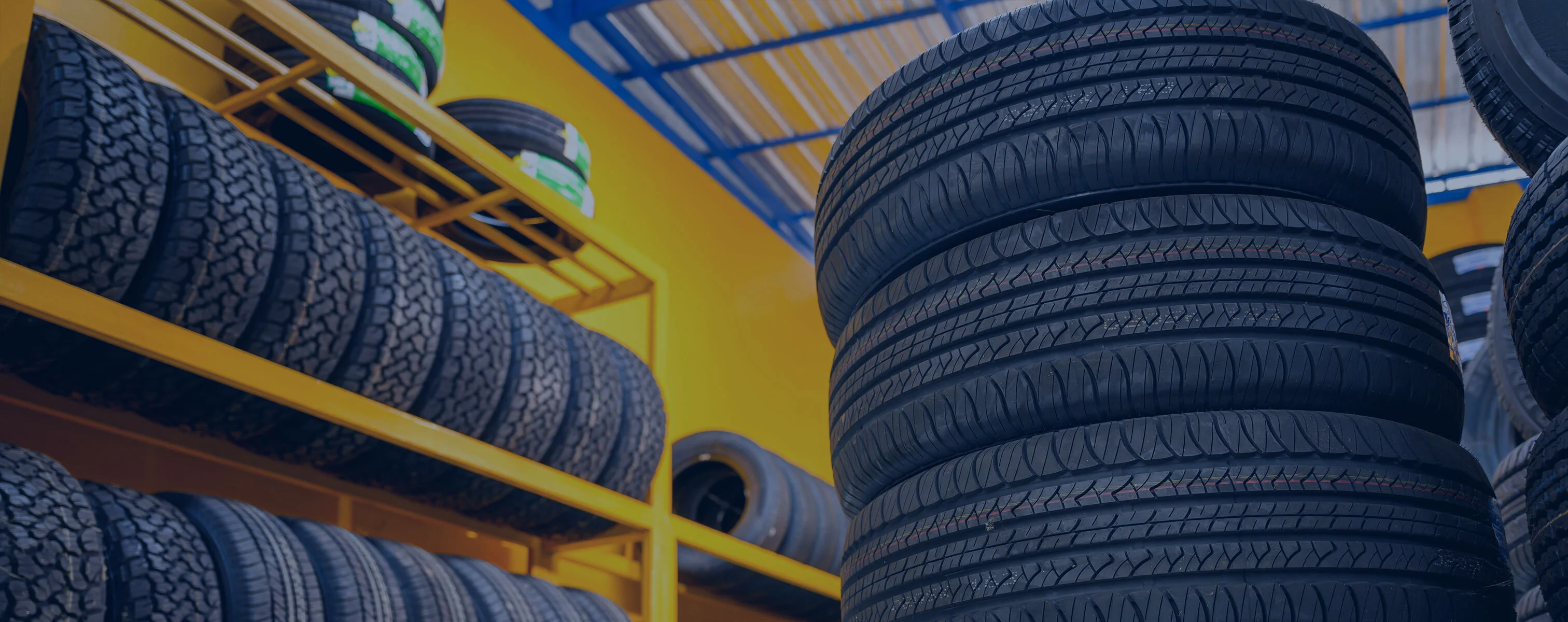 Opony samochodowe ułożone i spiętrzone w garażu o żółtych ścianach.