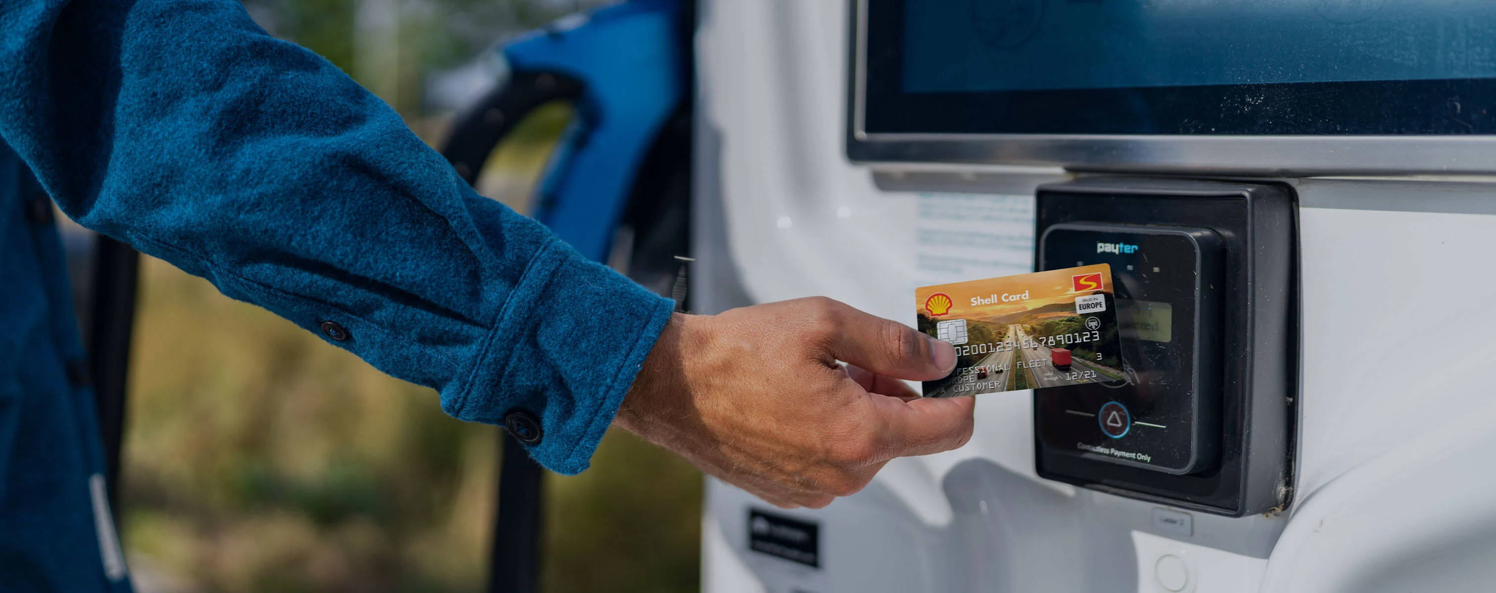 Eine Hand hält eine Shell-Karte an ein Lesegerät einer Ladestation für Elektroautos.