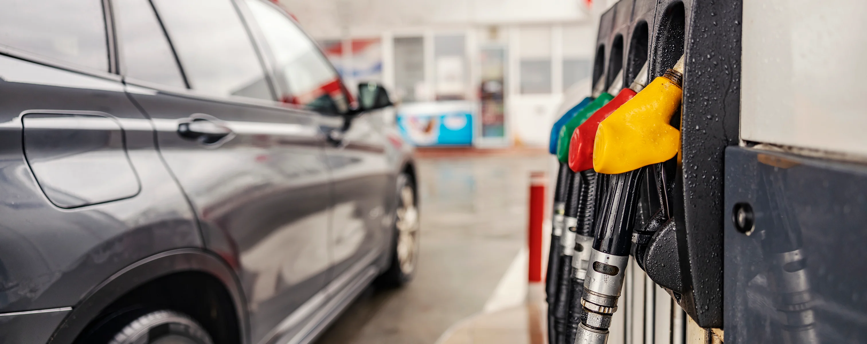 Tankstelle mit Zapfsäulen im Vordergrund und einem grauen Pkw beim Tanken im Hintergrund.