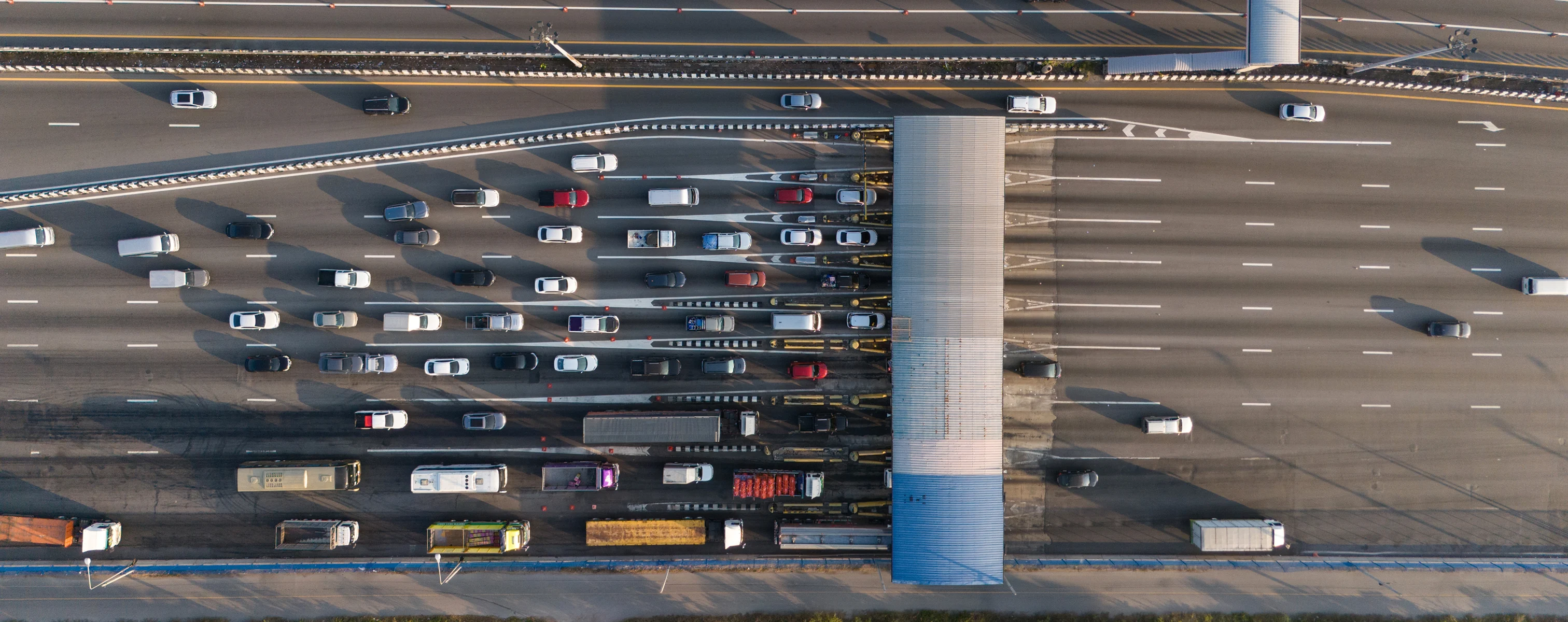 Luftaufnahme einer Mautstation auf einer mehrspurigen Autobahn mit Pkw und LKW.