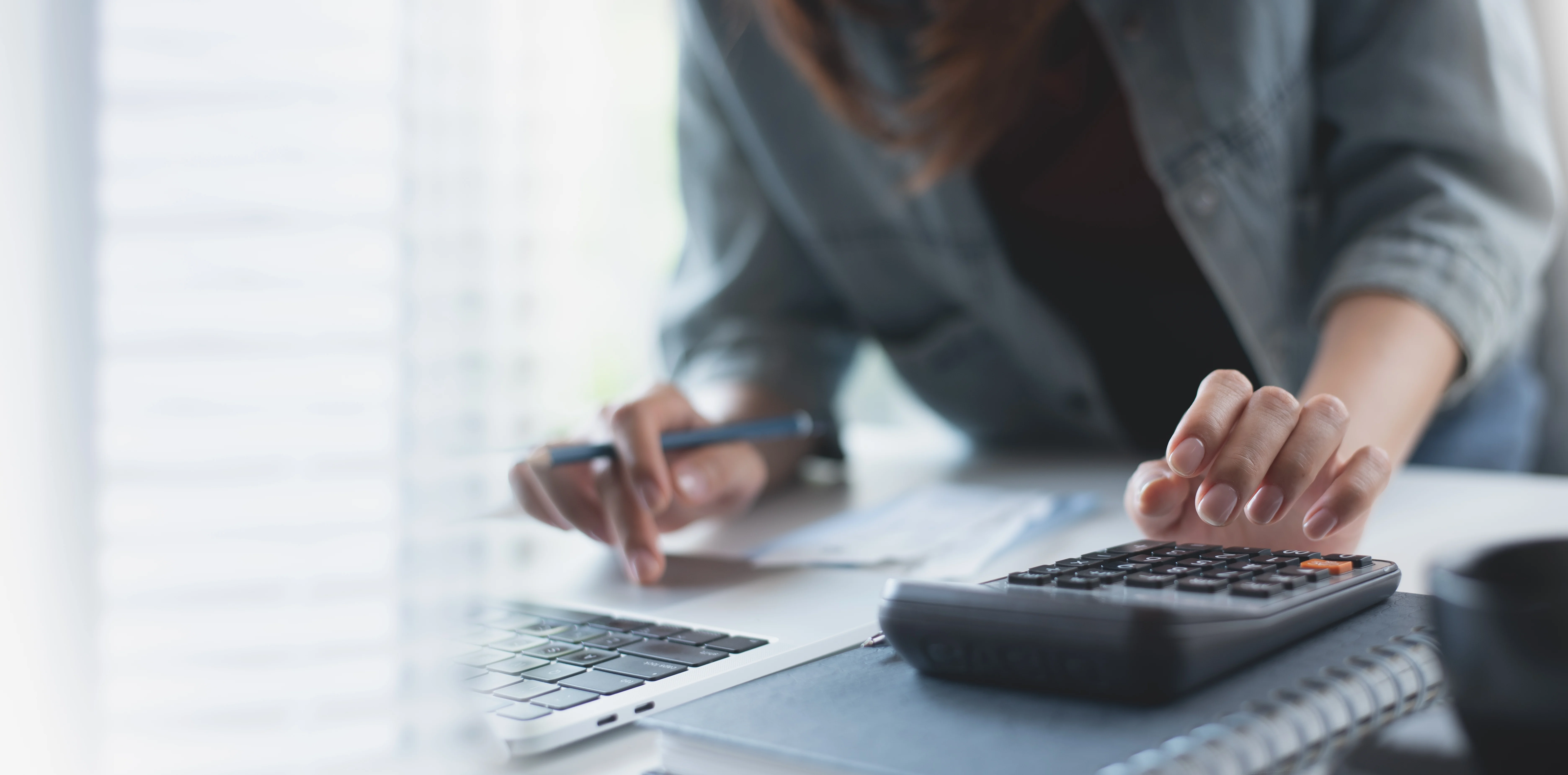 Persoon berekent financiën met een rekenmachine en laptop.