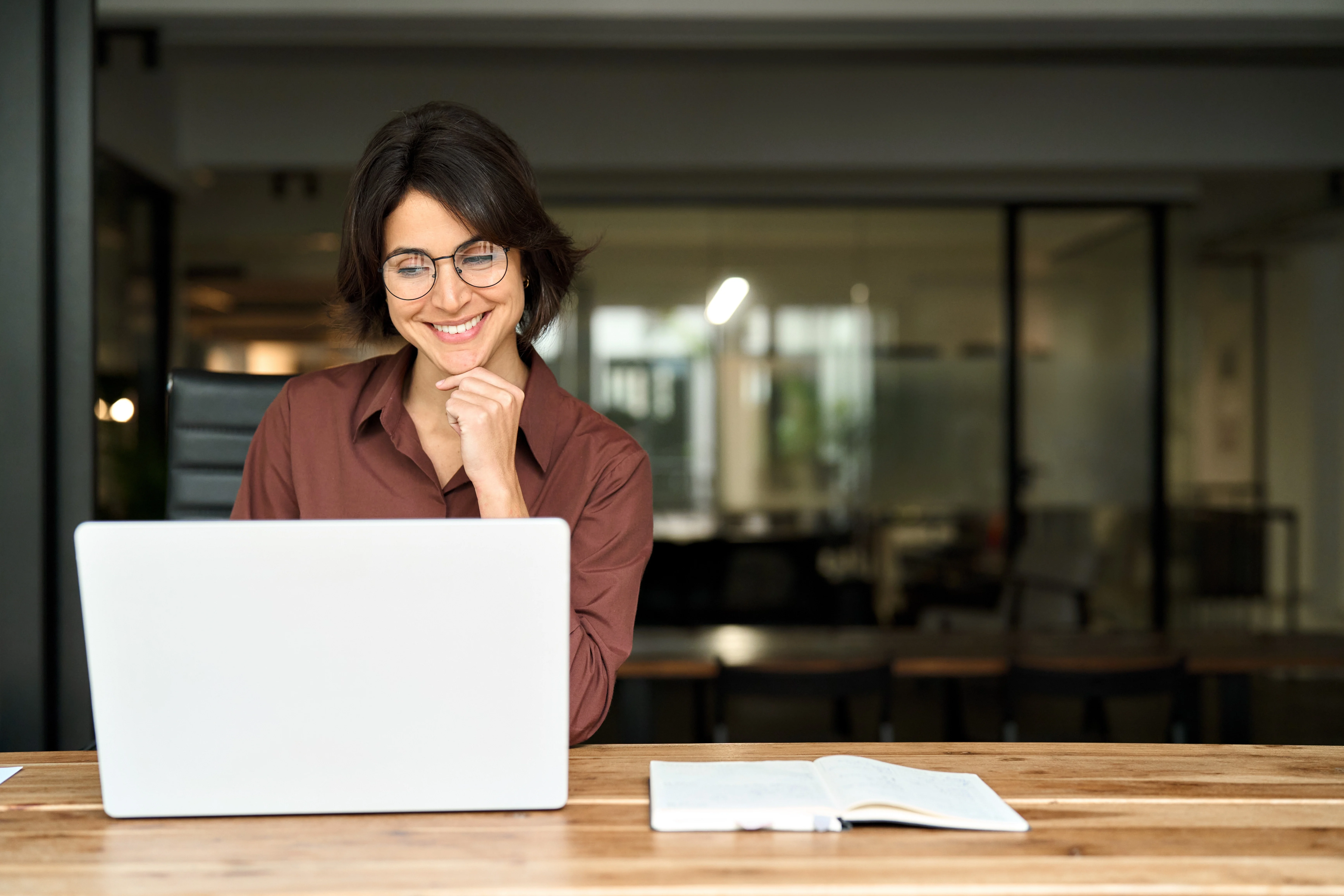 Une femme souriante est assise à un bureau et travaille sur son ordinateur portable.