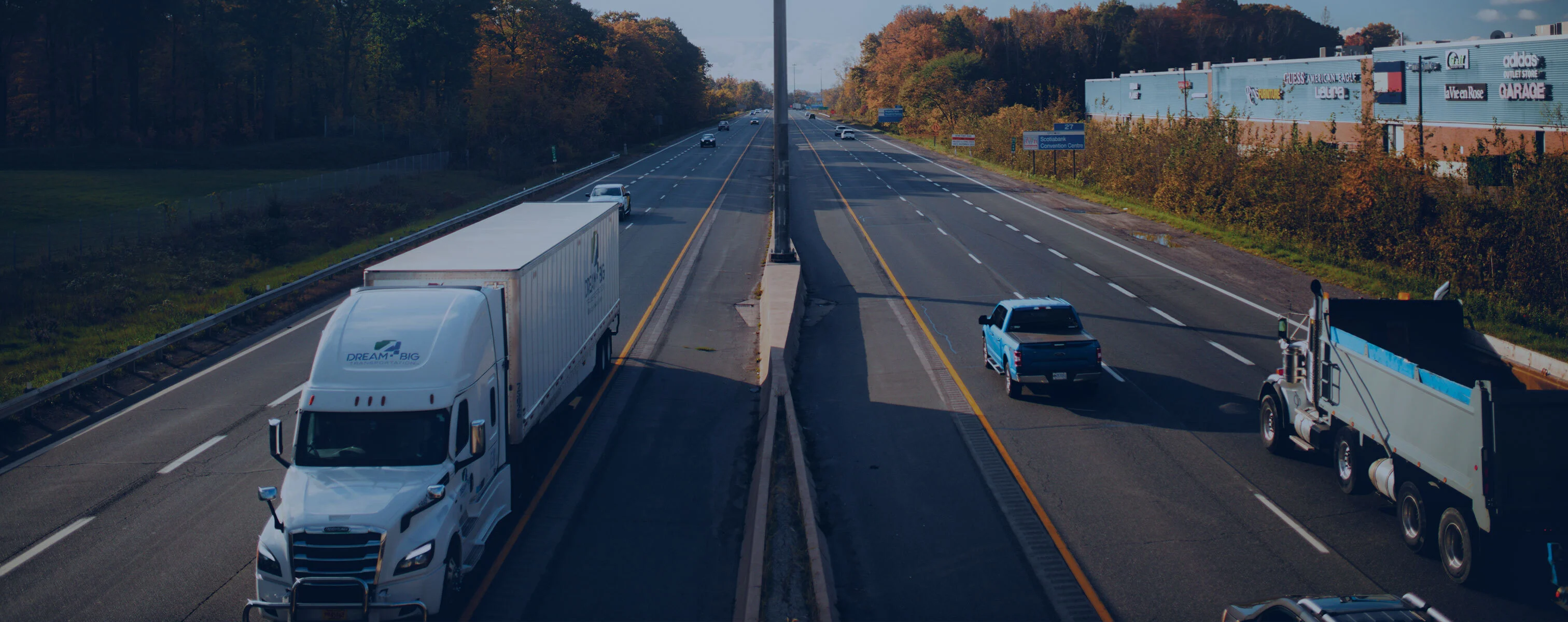 Des camions et des voitures roulent sur une large autoroute par une journée ensoleillée.