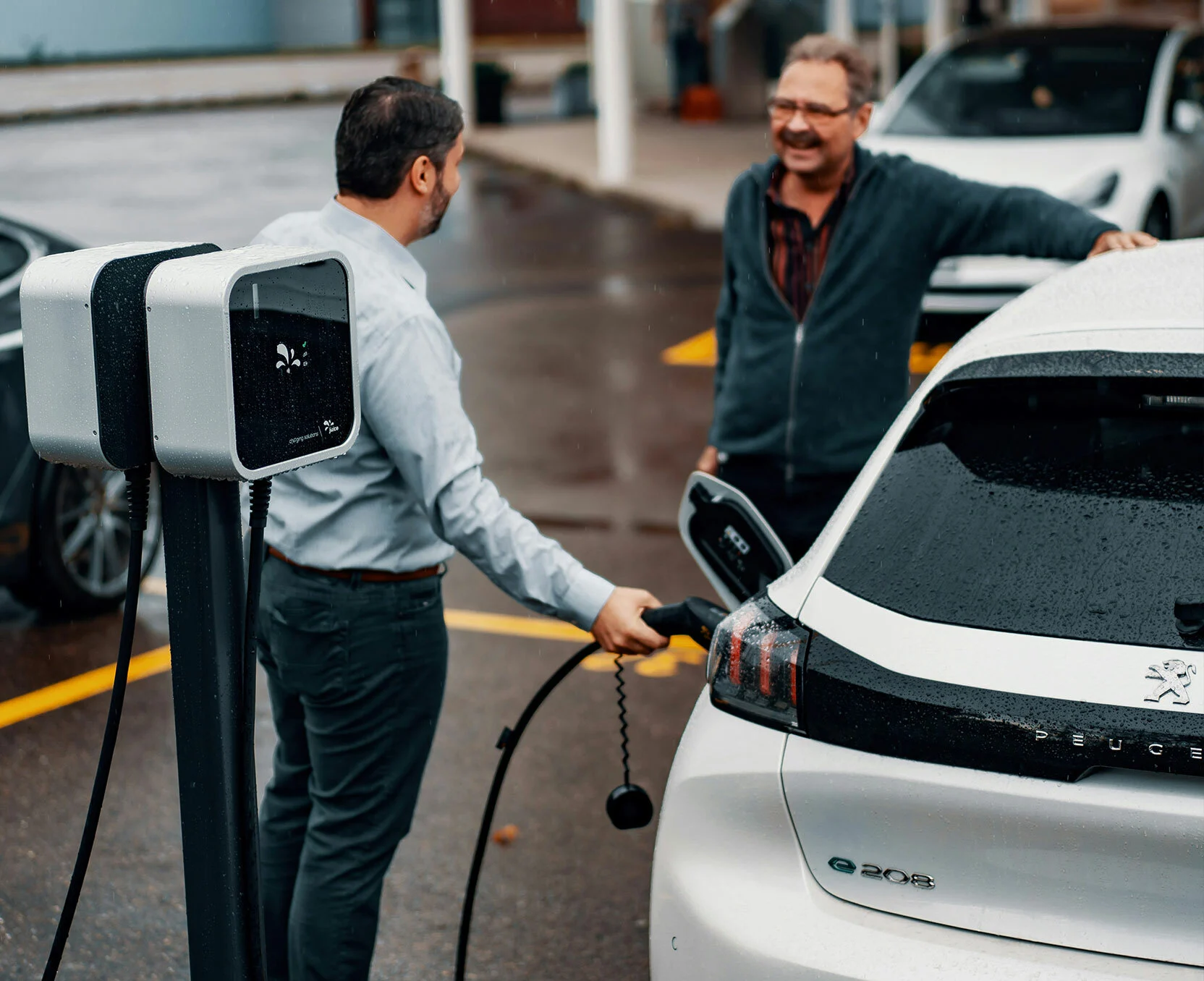Twee mannen laden een elektrische auto op in de regen.