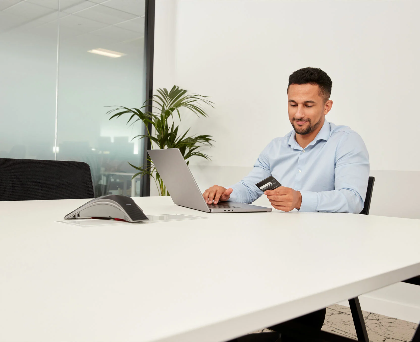 Man houdt een creditcard vast en werkt op zijn laptop op kantoor.