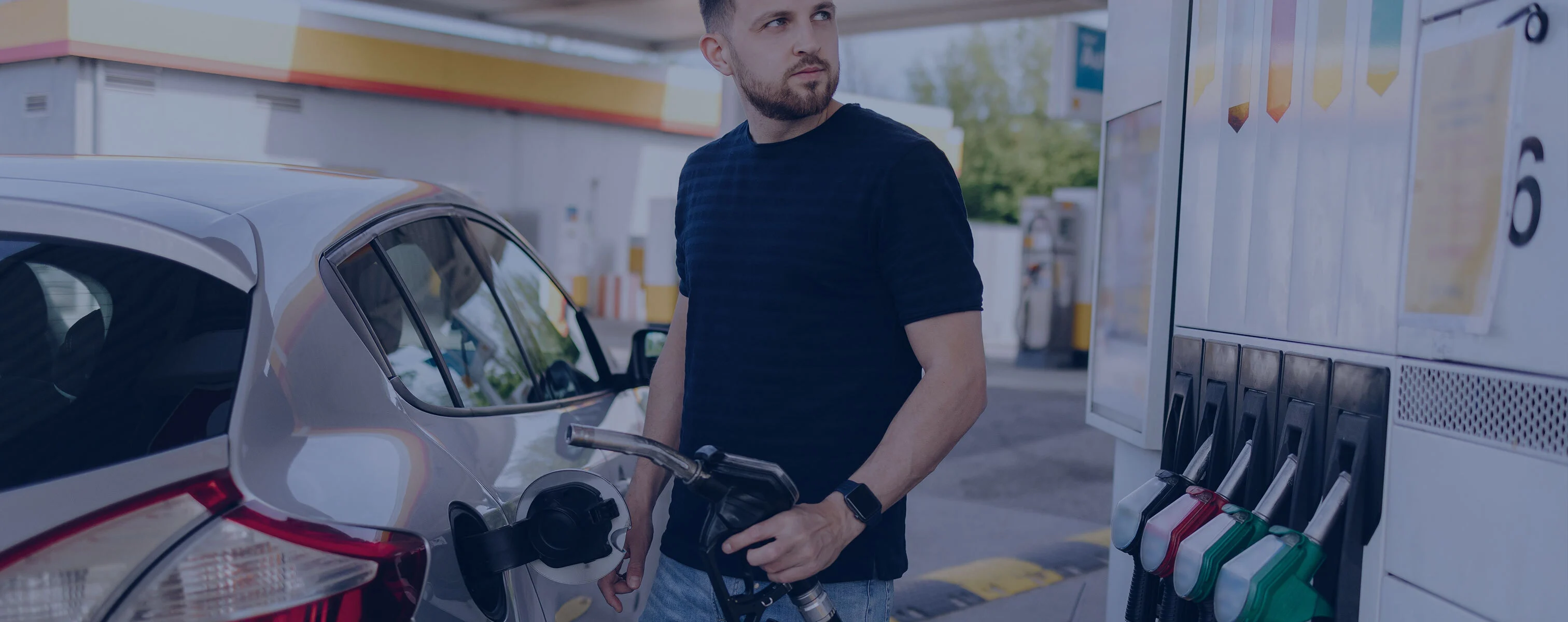 Een man in een zwart T-shirt tankt zijn auto bij een tankstation.