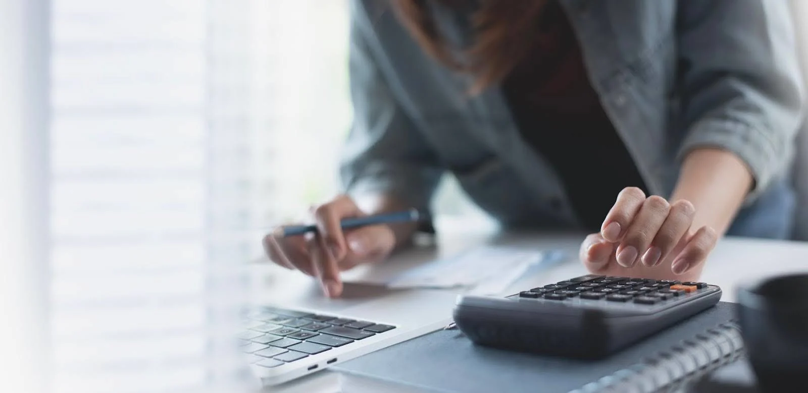 Persoon berekent financiën met een rekenmachine en laptop.