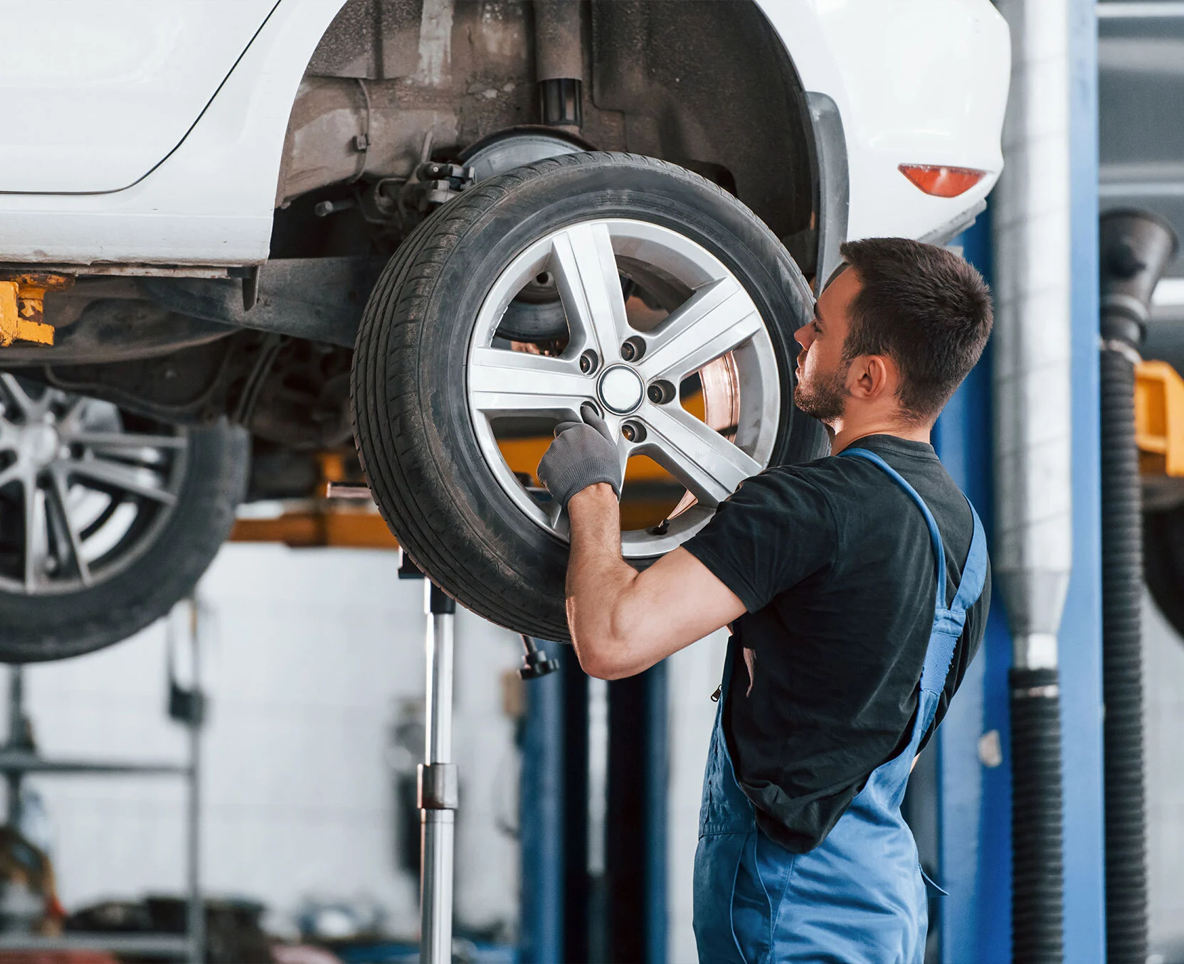 Un mécanicien garagiste en tenue de travail change les pneus usagés d’un véhicule.