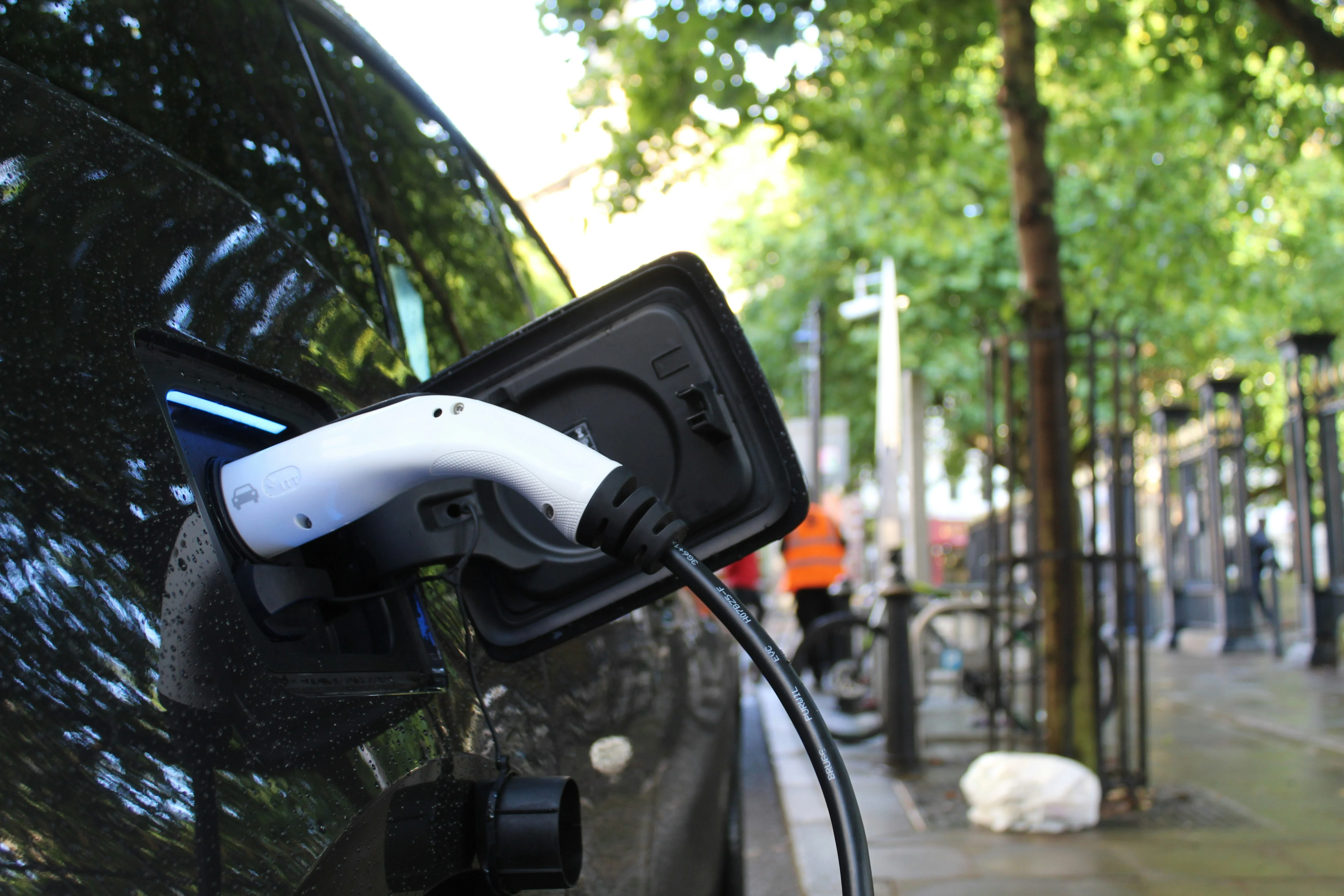 Een witte EV-laadstekker is aangesloten op een zwarte auto in een met bomen omzoomde straat in de stad