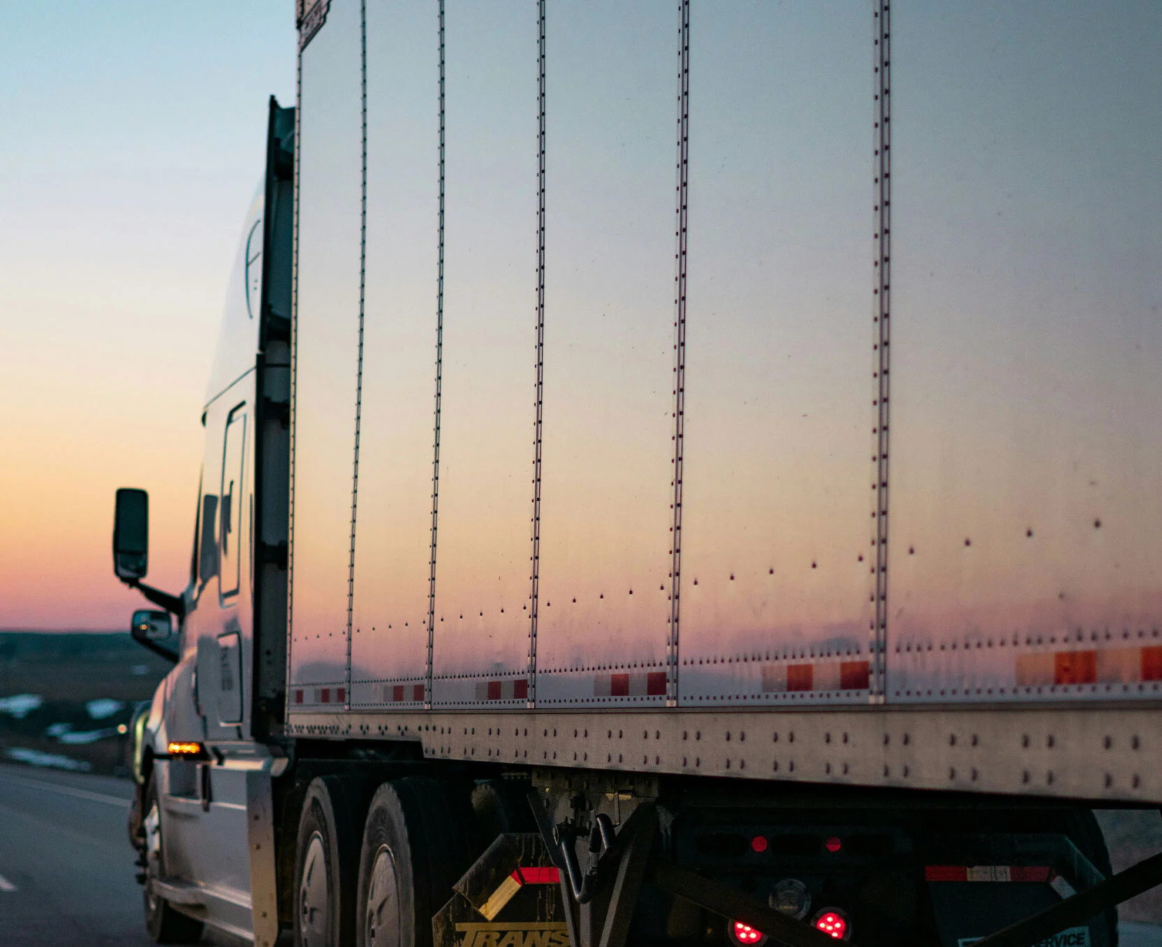 Zijkant van een vrachtwagen die bij zonsondergang over de snelweg rijdt.