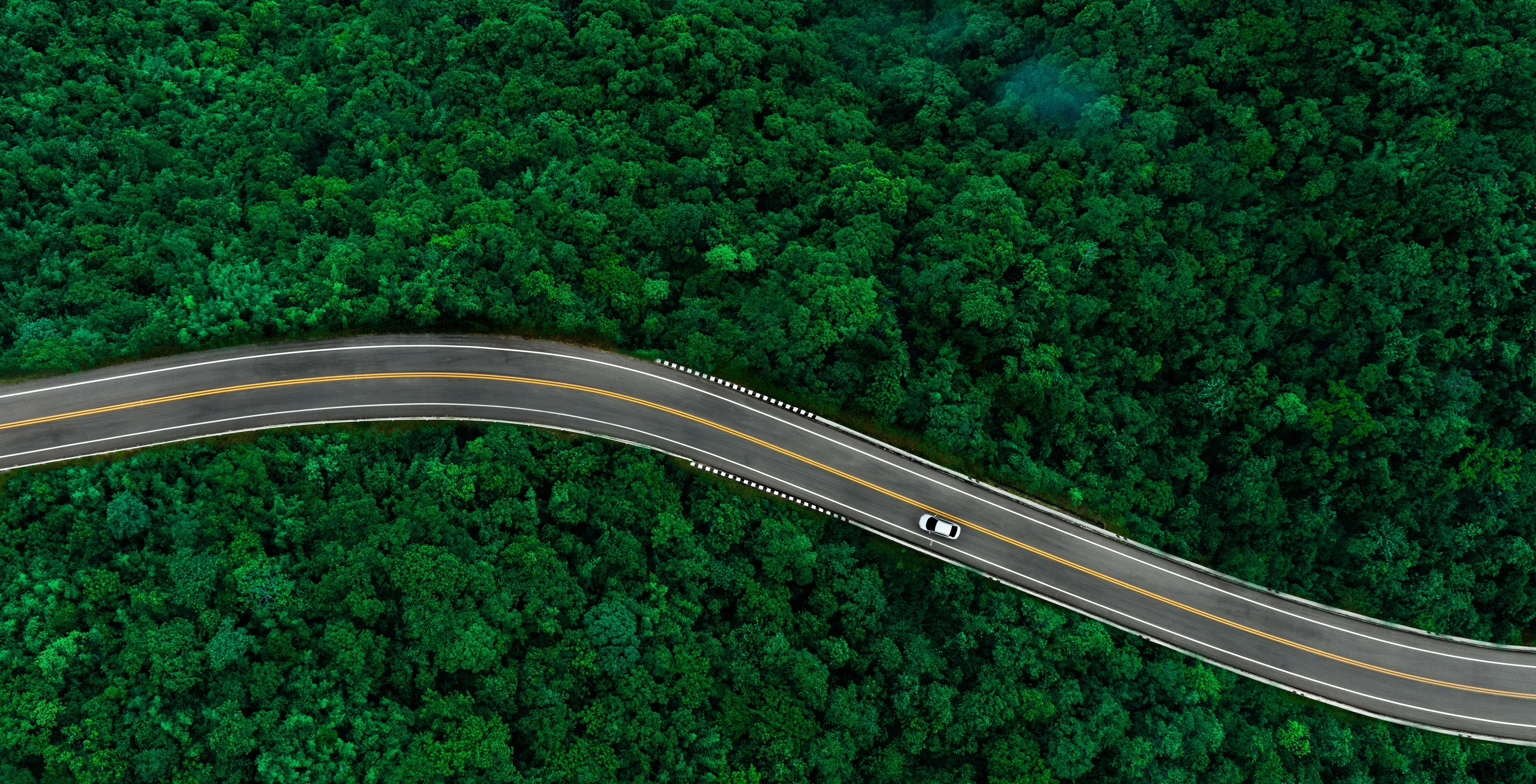 Vue aérienne d'une route sinueuse entourée de forêt dense.