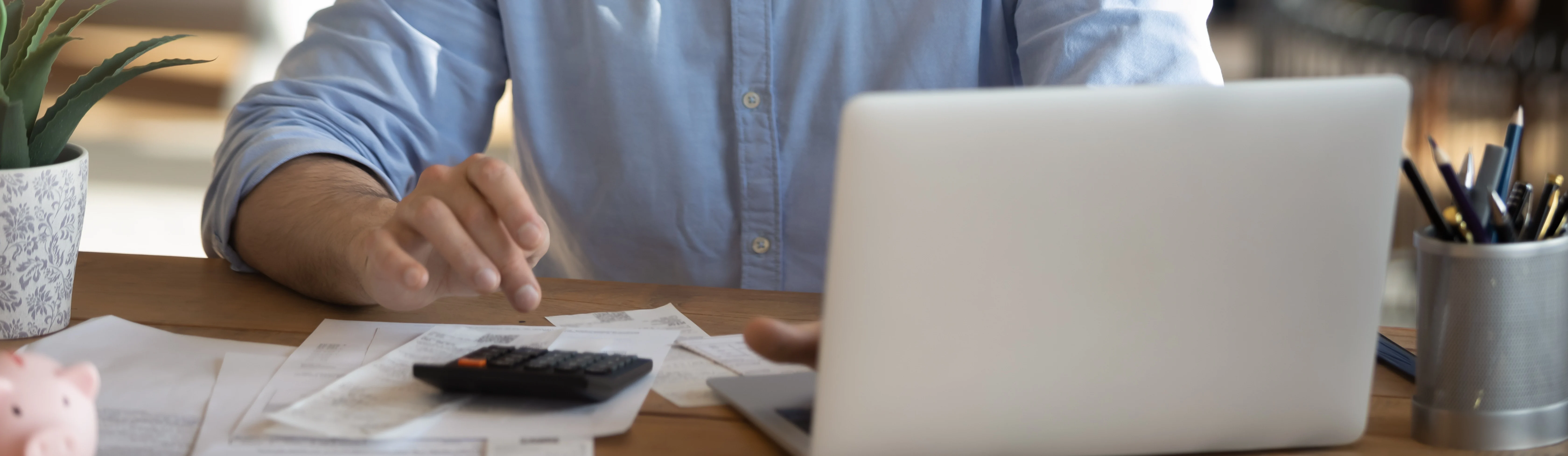 Mężczyzna w okularach pracuje przy biurku z laptopem, dokumentami i kalkulatorem