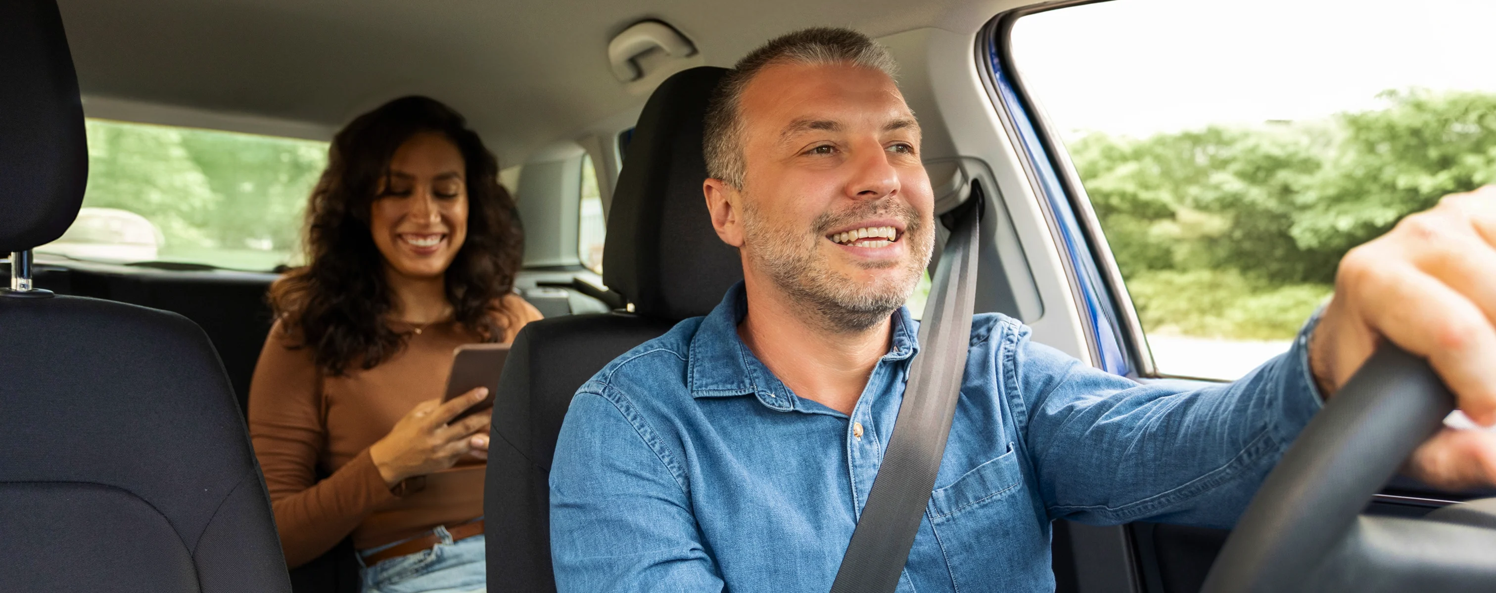 Taxifahrer im Einsatz mit Fahrgast auf dem Rücksitz, die während der Fahrt ihr Smartphone nutzt
