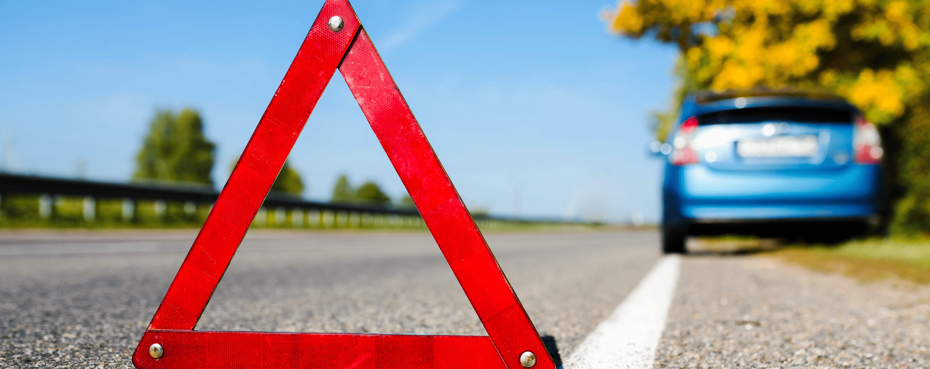 Rotes Warndreieck auf einer Straße neben einem liegen gebliebenen blauen Auto.