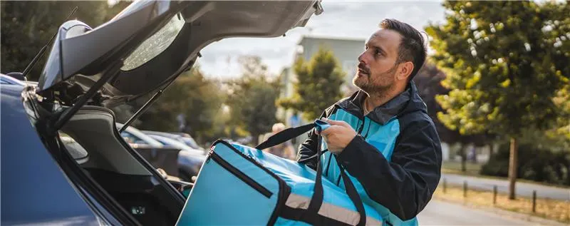 Lieferdienst-Fahrer nimmt Thermotasche aus dem Auto für Essenslieferung