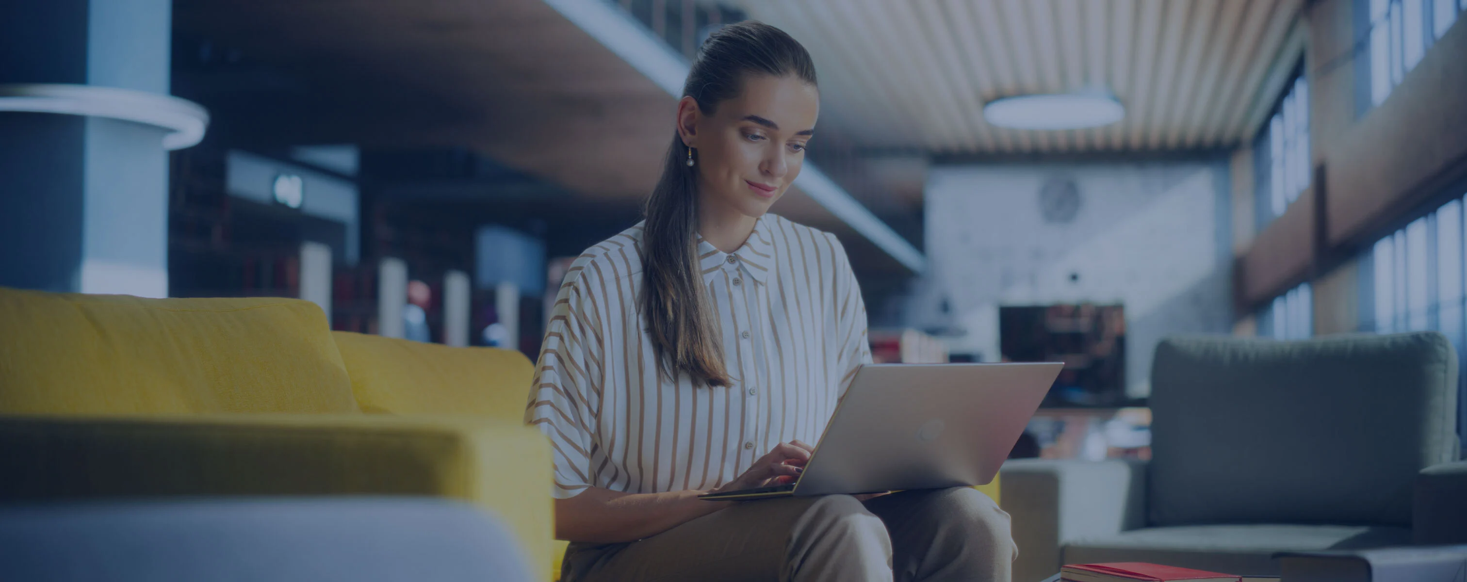 Une femme travaille sur son ordinateur portable dans un bureau moderne, assise sur un canapé.
