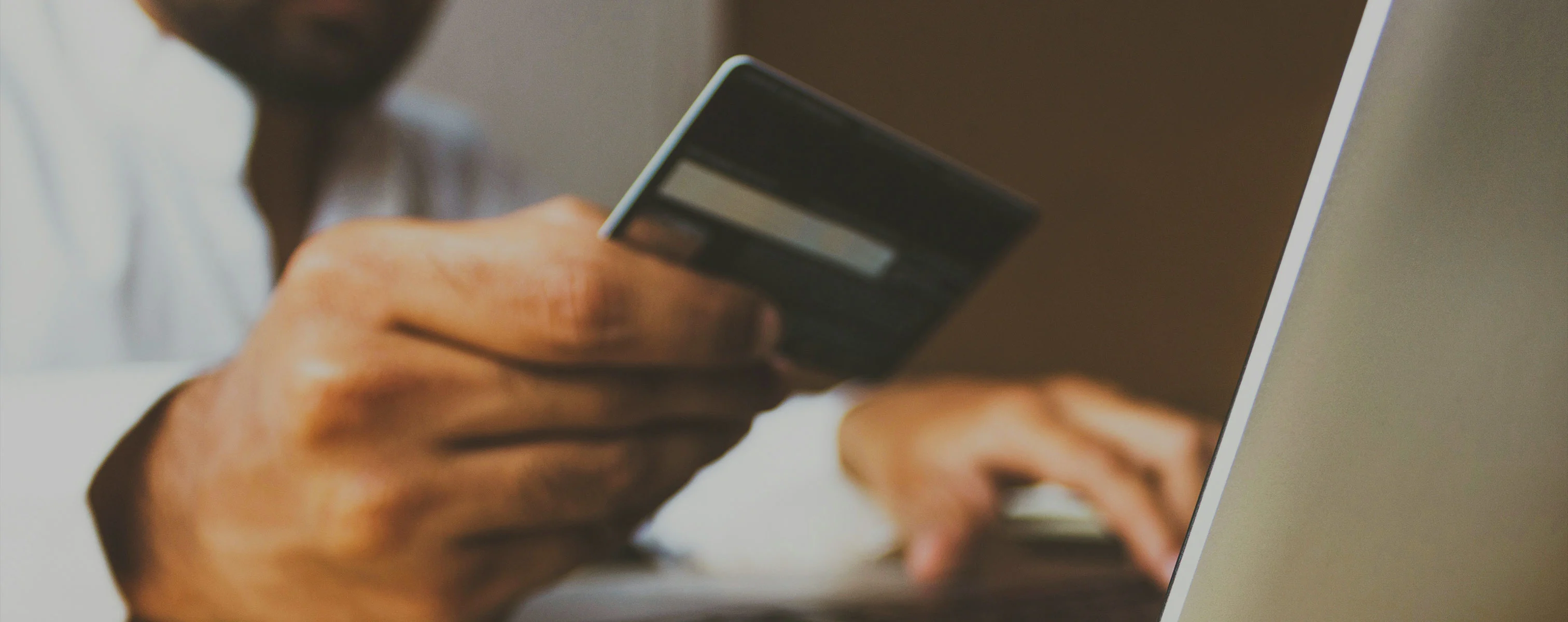 Een persoon die een creditcard vasthoudt terwijl hij op een laptop werkt.