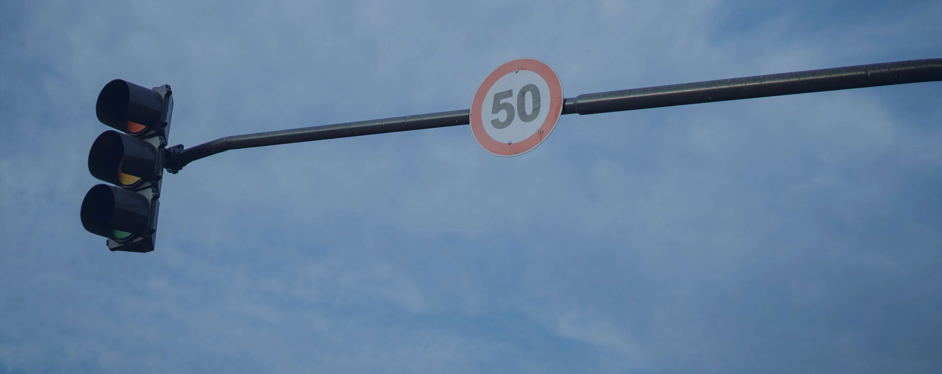 Sygnalizacja świetlna obok znaku drogowego wskazującego ograniczenie prędkości do 50 kilometrów na godzinę na tle błękitnego nieba.