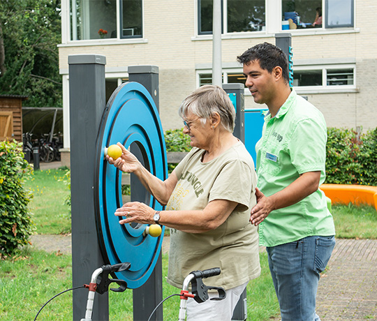 Senior woman using exercise equipment with assistance from a caregiver at Norschoten Care Organization.