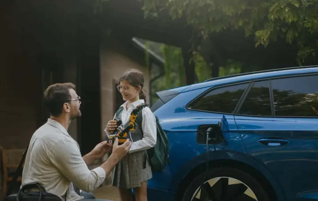 Un père, agenouillé, parle à sa fille pendant que sa voiture électrique est en train de se recharger à côté.