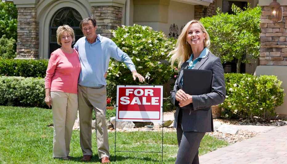 Couple with agent standing in front of for sale sign.