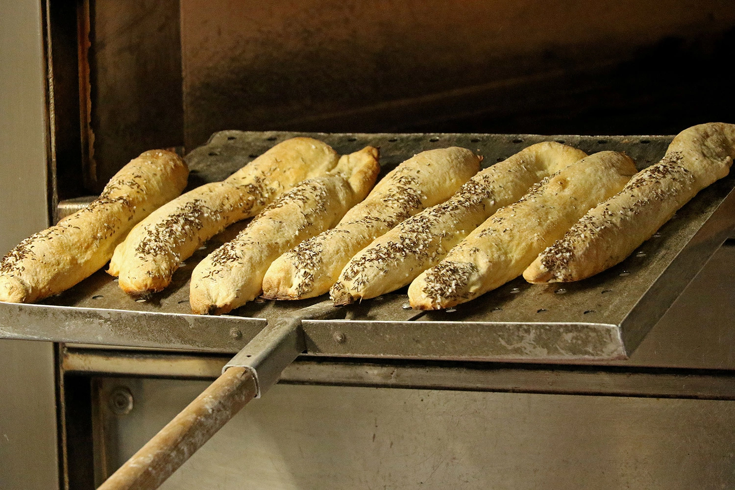 Several souls breads are placed on a large oven slide and pushed into the oven.