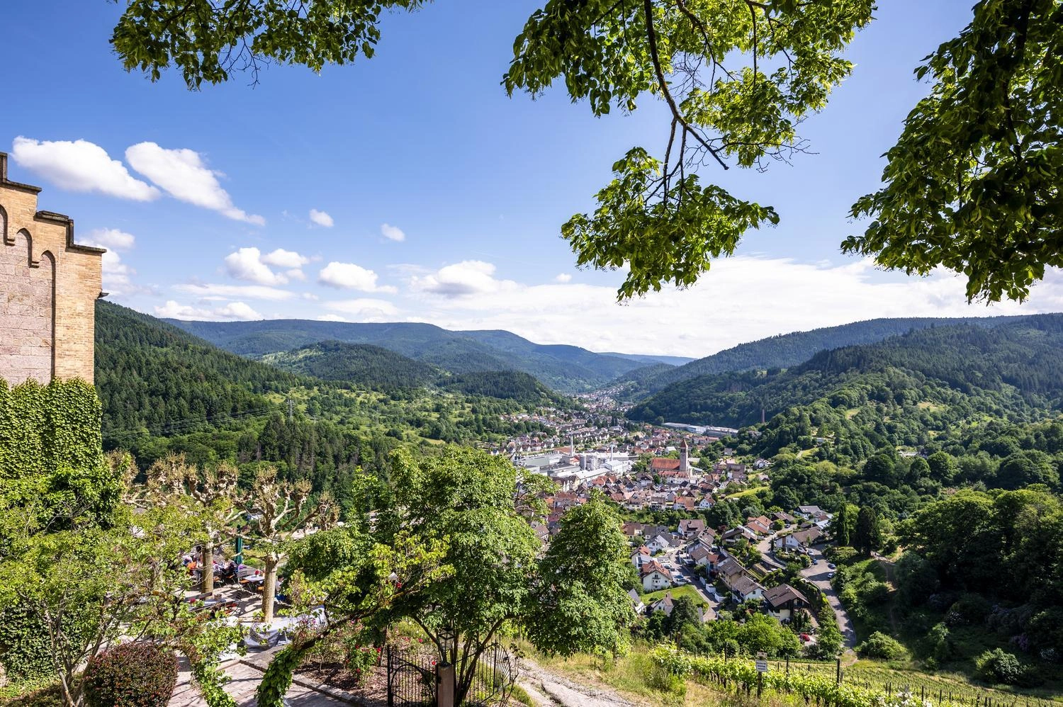 Panoramablick auf Gernsbach im Schwarzwald mit roten Dächern, eingebettet zwischen grünen Hügeln und Wäldern unter blauem Himmel mit Wolken.