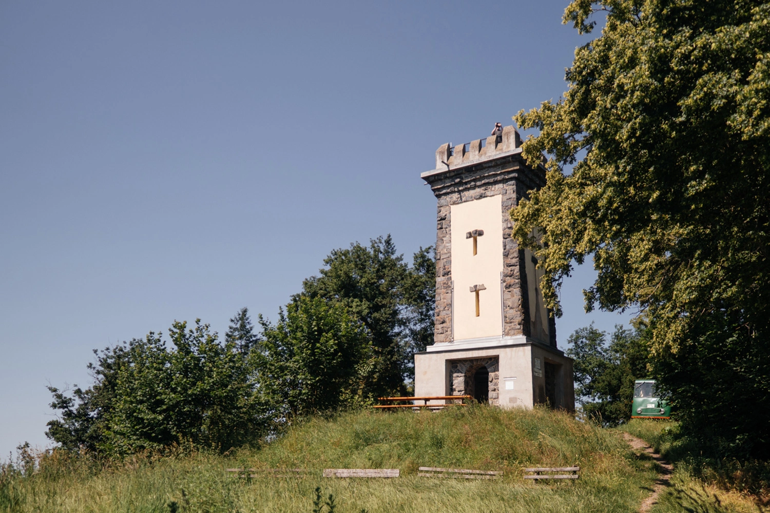 The Skull Tower on the Kaiserstuhl stands on a wooded hilltop, featuring a bench and a trail leading up to it. 