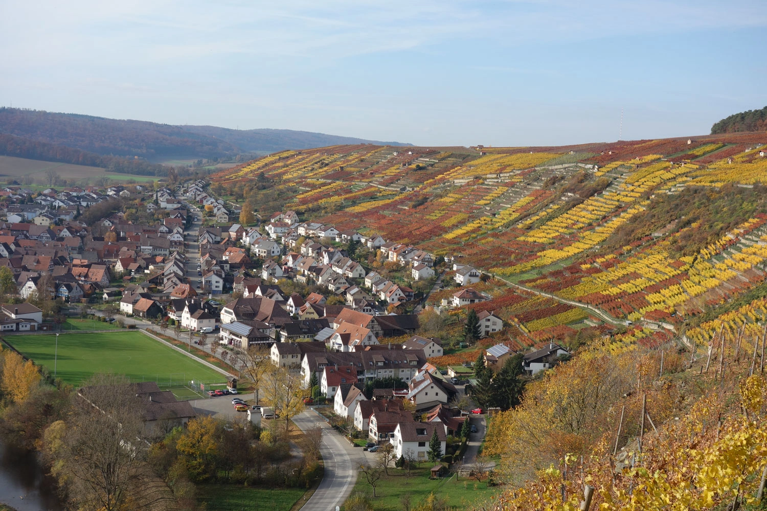 View over the steep slopes in Rosswag. On the left is a village with houses. The vineyards on the right are colourful from autumn.