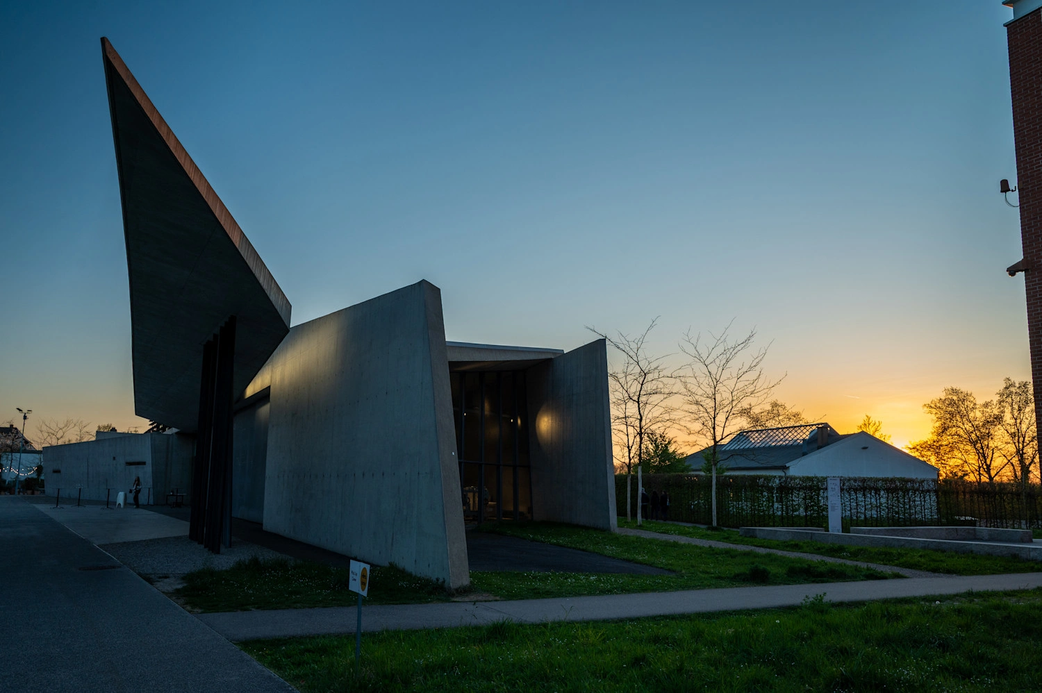 Gebäude mit Betonfassade im Sonnenuntergang. An der linken Seite ragt eine Spitze in den Himmel.