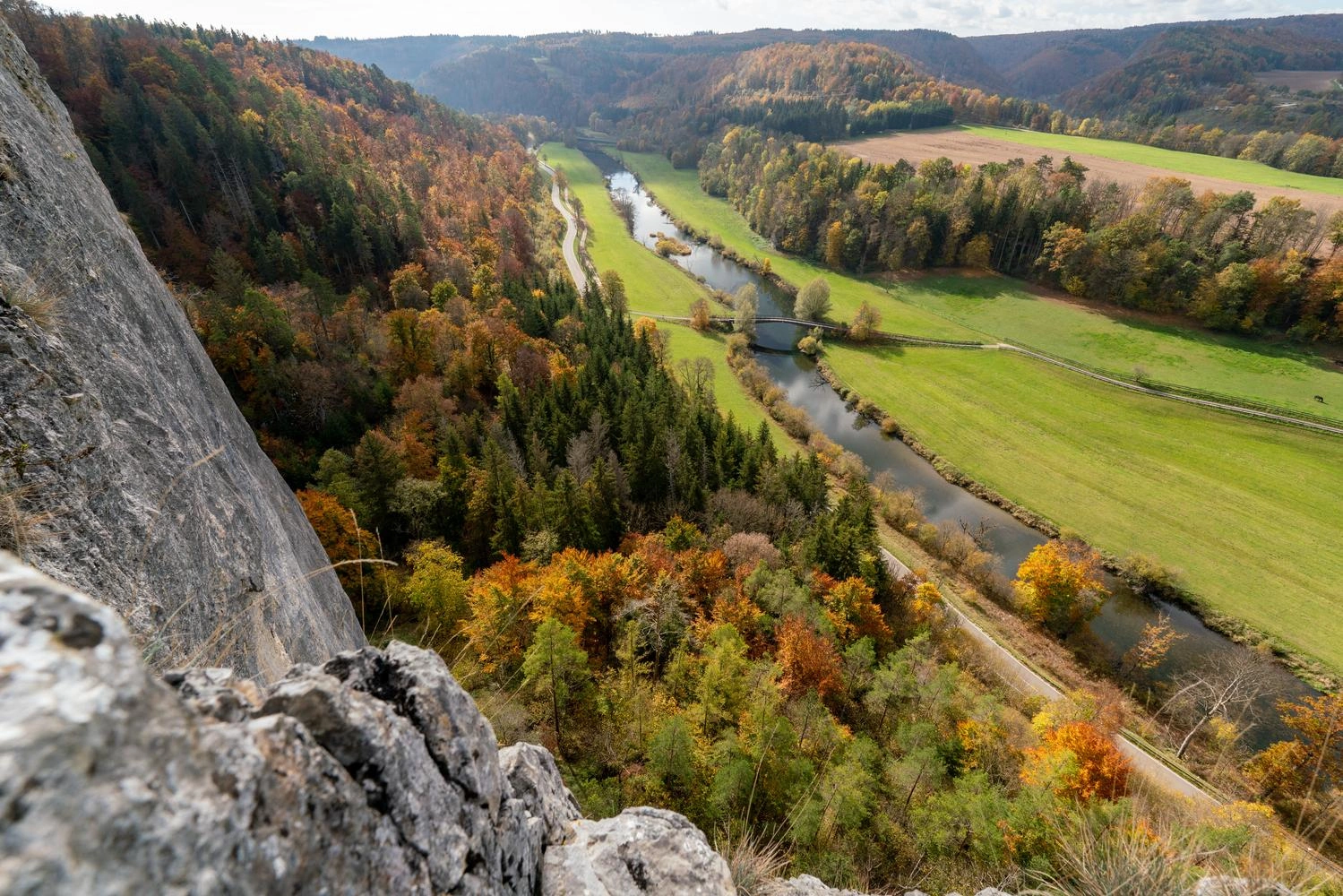 In the foreground is the rock face, behind it the view opens up over a wide valley through which the Danube flows.