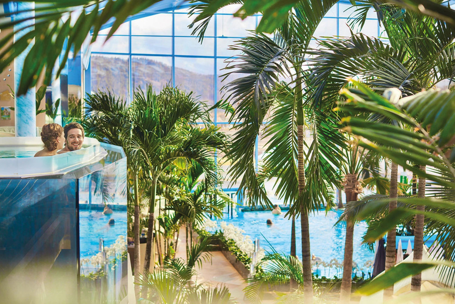 Überblick über das Indoor-Badeparadies mit verschiedenen Schwimmbecken und vielen Palmen.