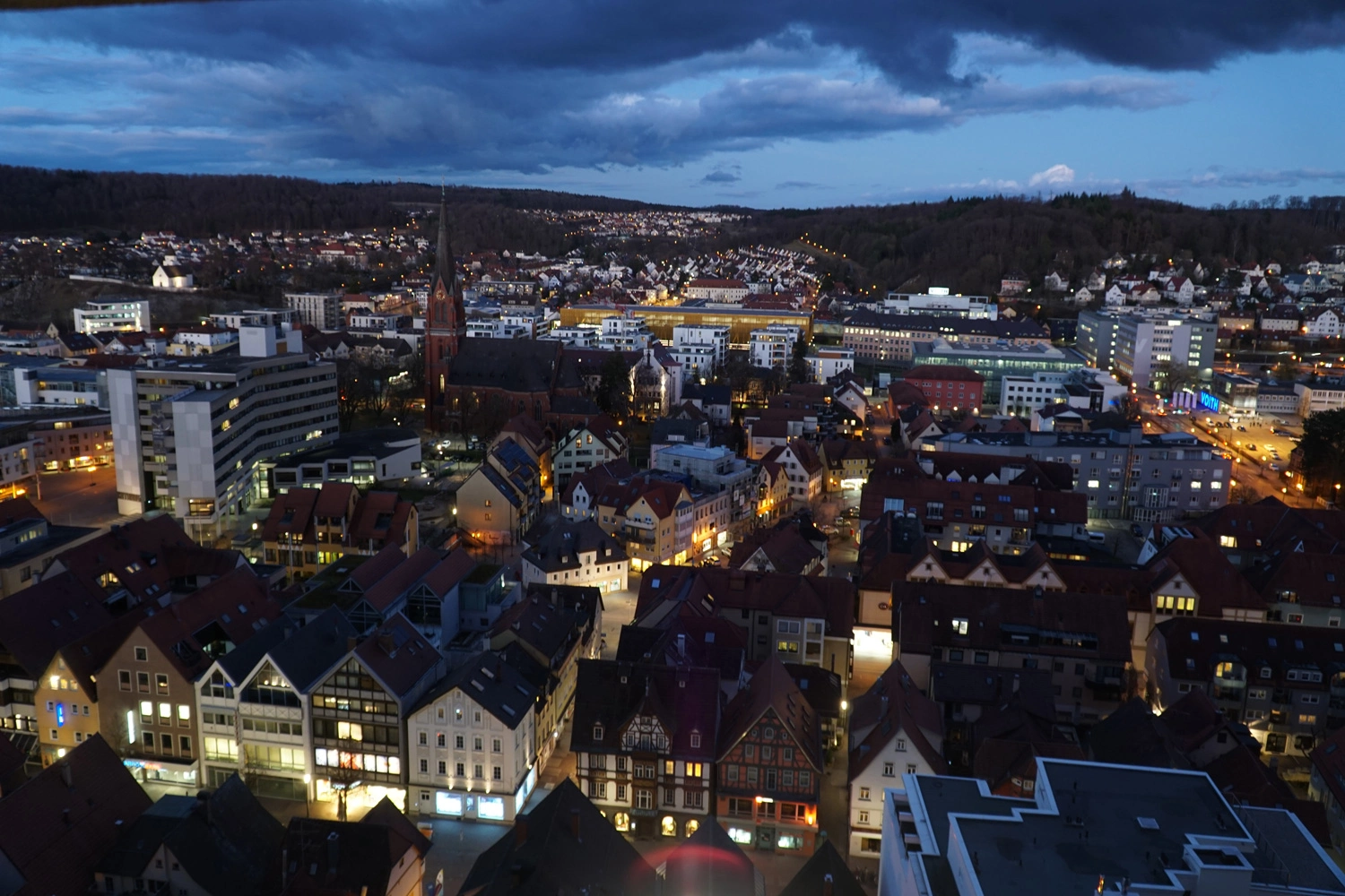 View from above over a city in the evening. The sky is dark and the city lights are shining.