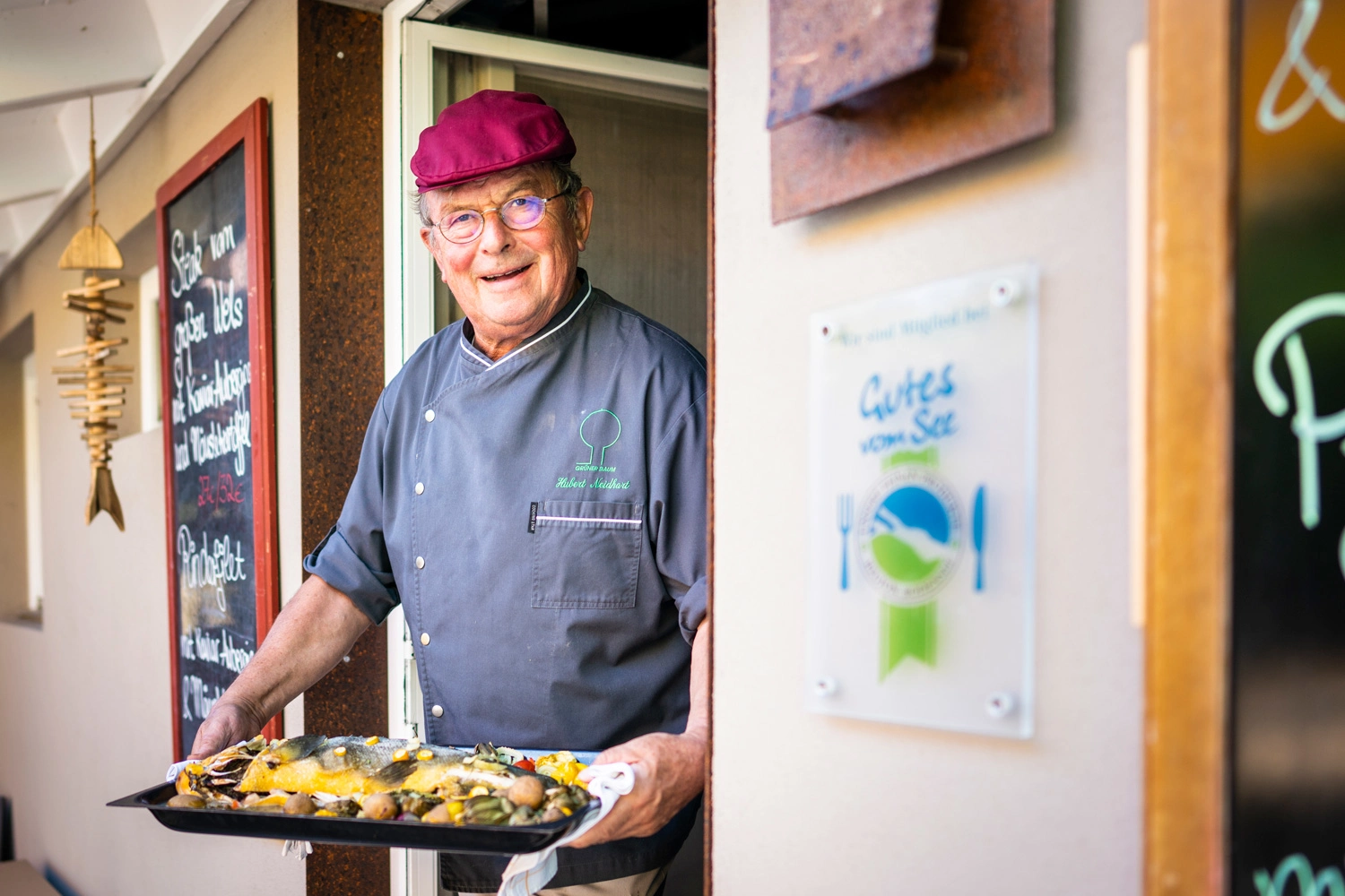 A chef comes out of his kitchen with a fish platter.