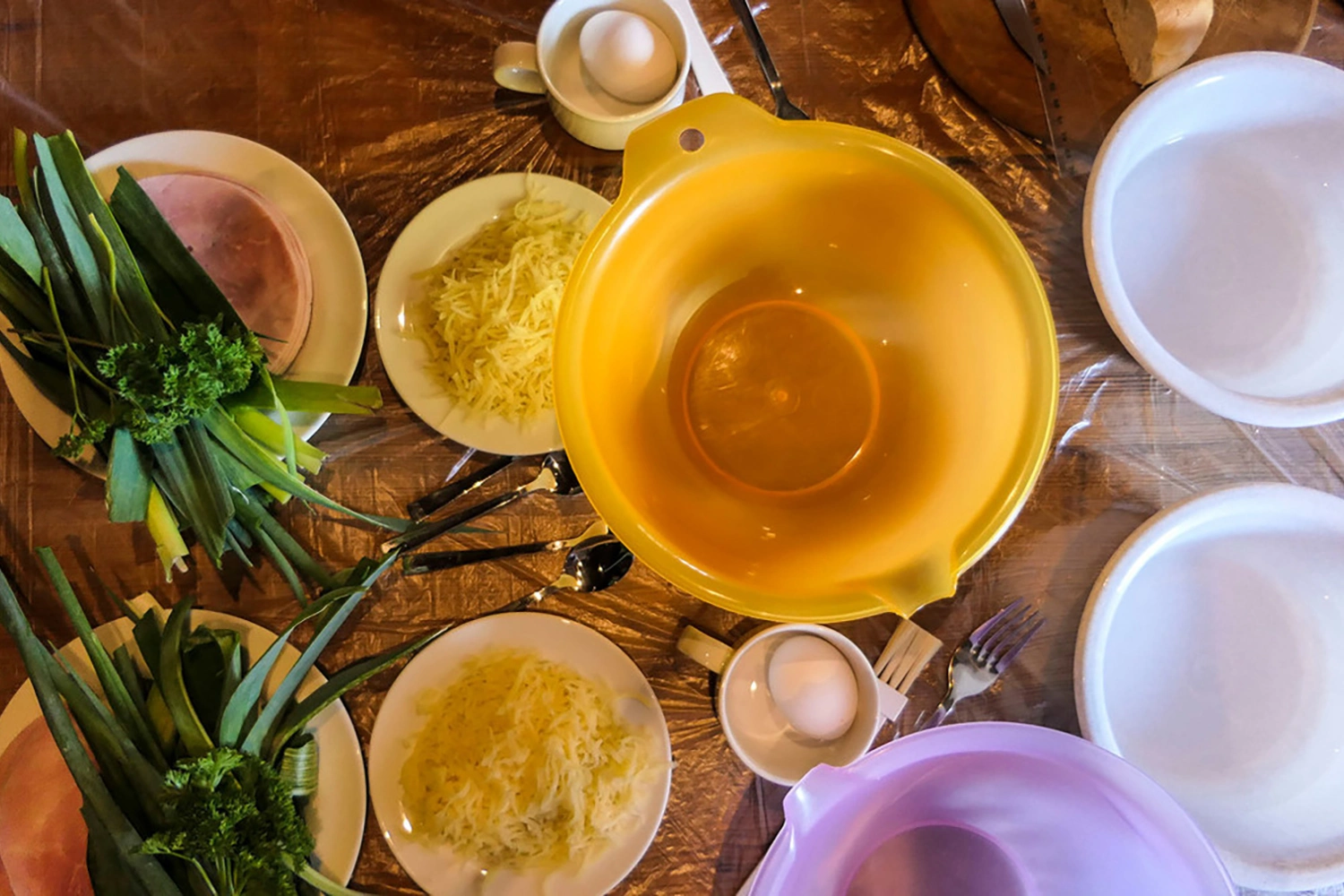 Ingredients and bowls for making Maultaschen together: leeks, parsley, ham, grated cheese and eggs arranged on a table.