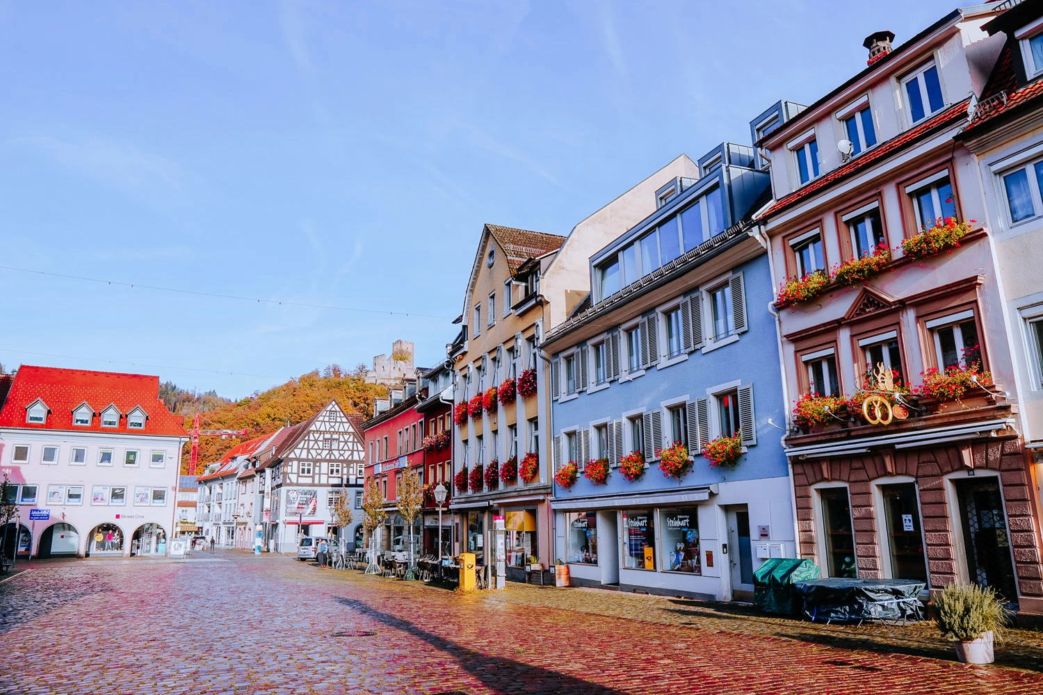 View over the market square in a small town. A castle on a wooded hill can be seen in the background.