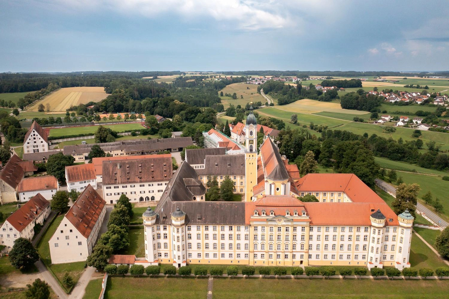 Luftaufnahme des barocken Klosters Ochsenhausen mit roten Dächern, umgeben von grünen Feldern und Wäldern in Oberschwaben.