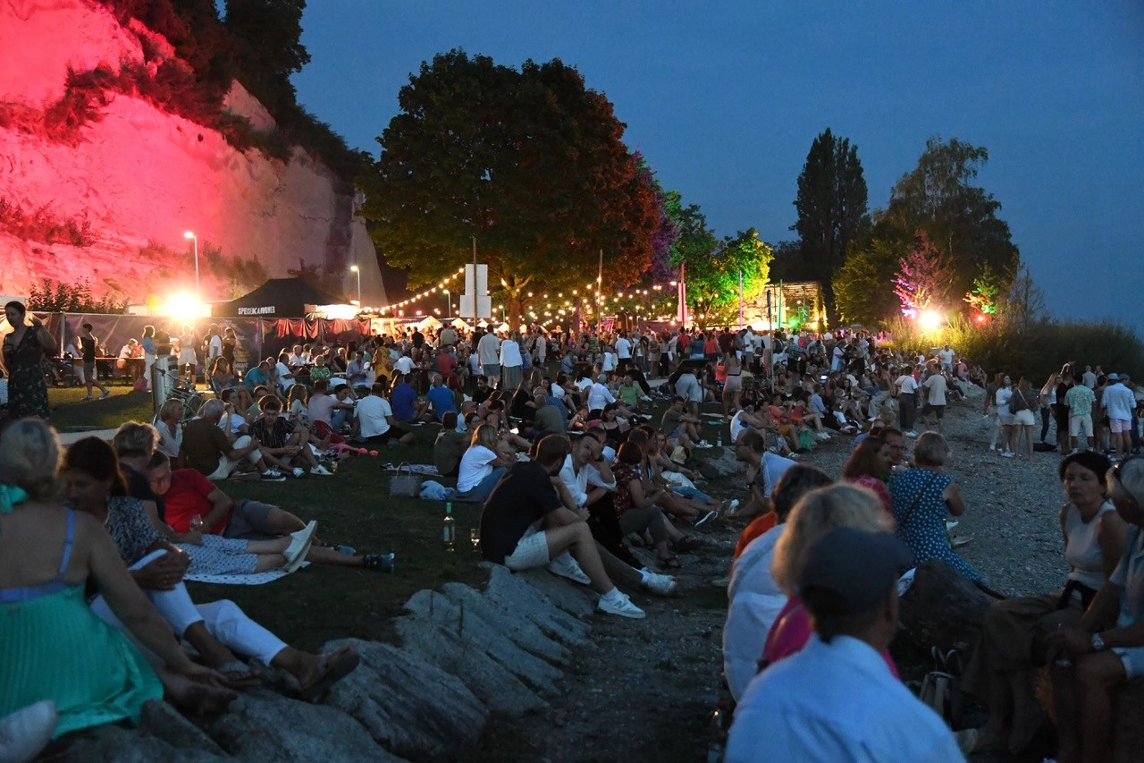 Viele Menschen sitzen bei Dunkelheit am Ufer eines Sees.