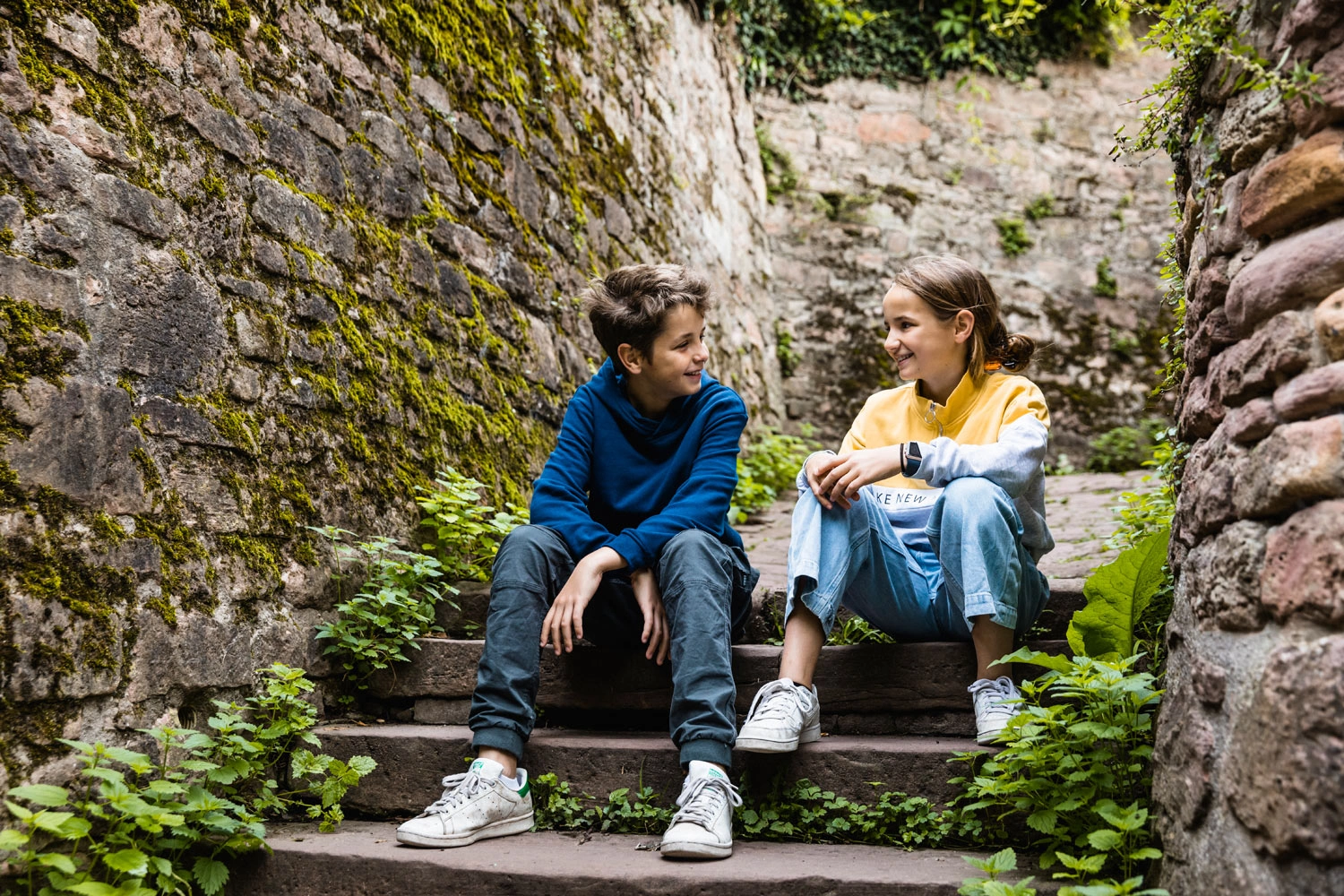 Ein Junge und ein Mädchen sitzen zusammen auf einer steilen Treppe. Rechts und links ragen alte Mauern empor.