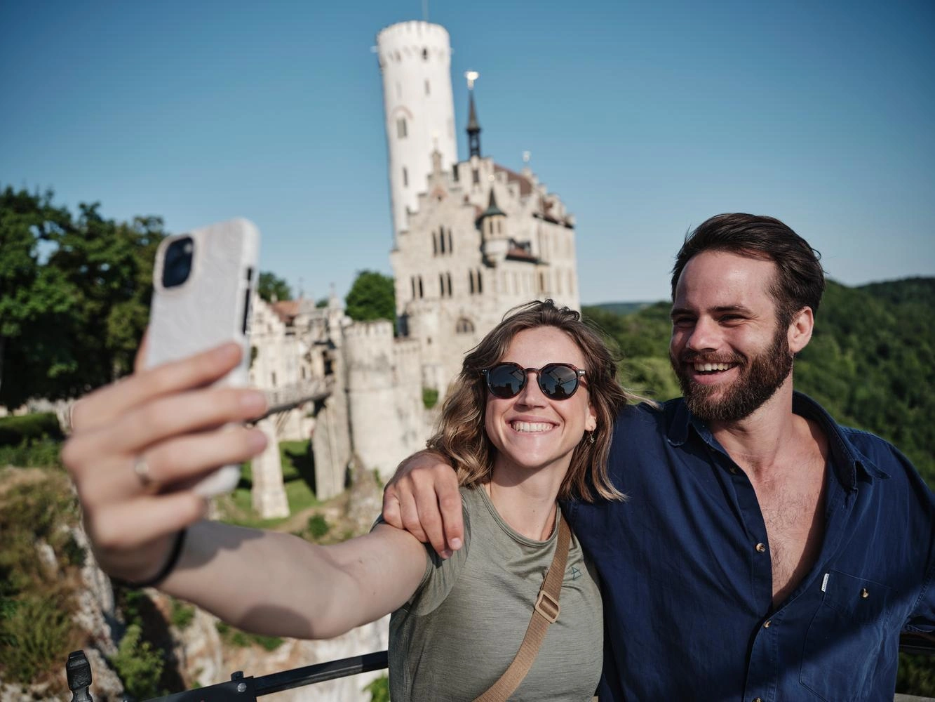 Two people are taking a selfie with Lichtenstein Castle in the background.