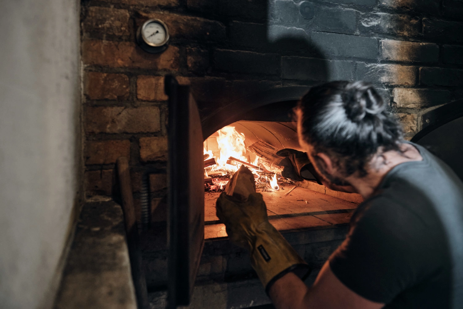 Ein Mann feuert einen Holzofen an und legt dafür Holz ins Feuern nach.