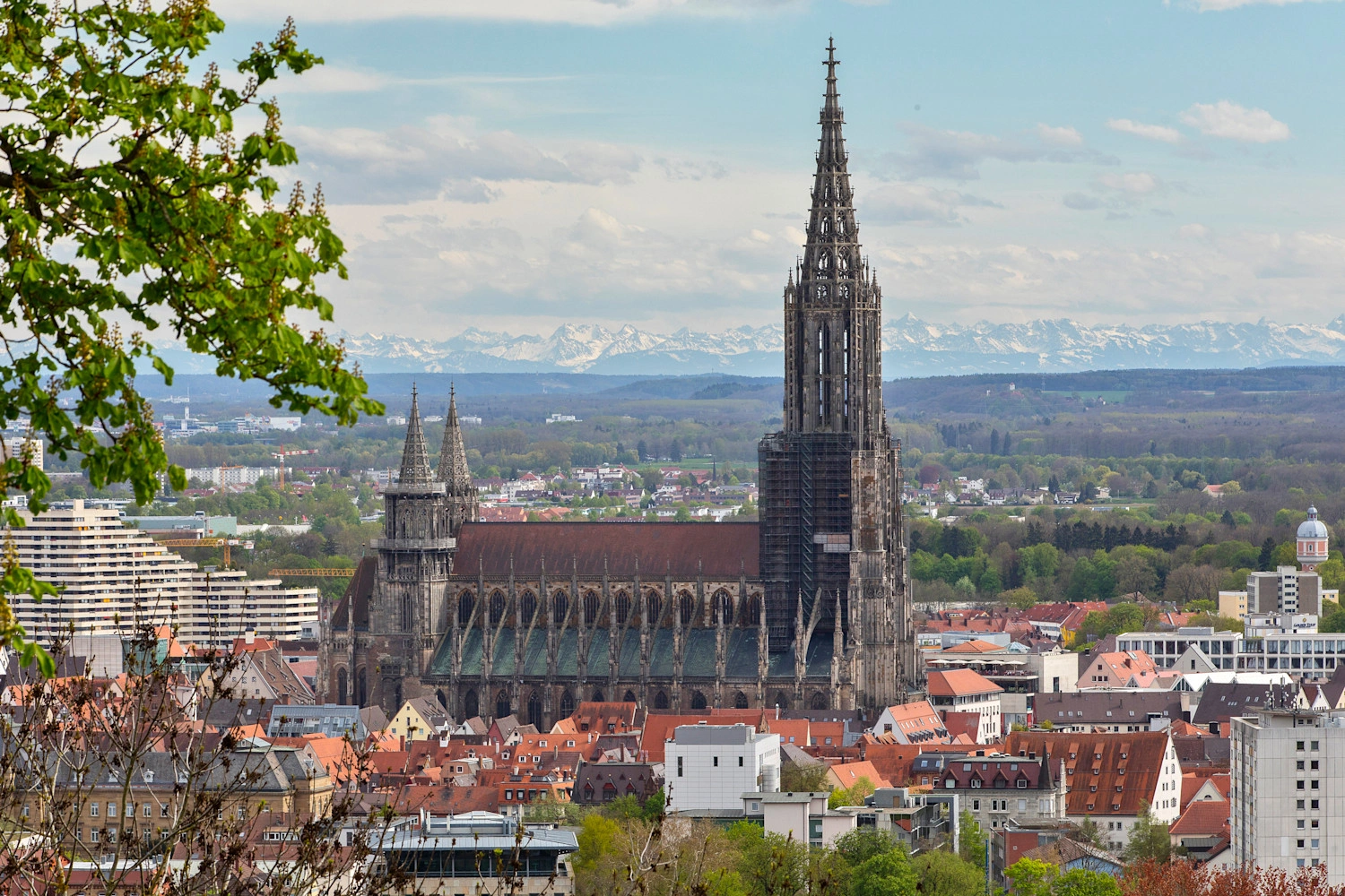 Ulm Minster stands out imposingly from the cityscape. In the distant background you can see mountains with snow-covered peaks.